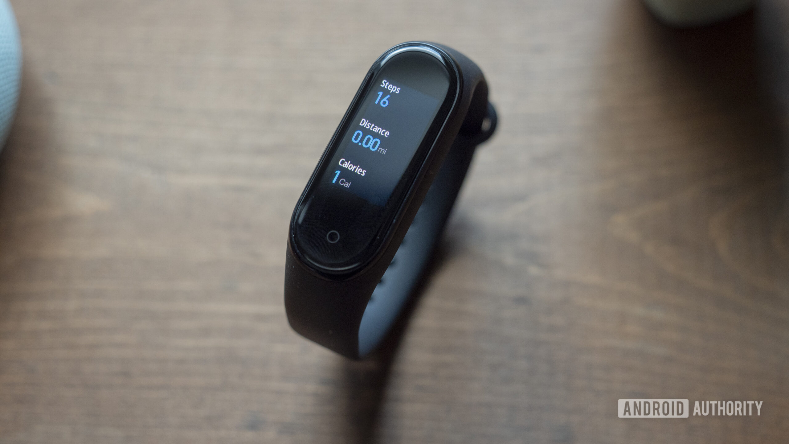 A Xiaomi Mi Band 4 rests on a tabletop displaying a user's steps, distance, and calories burned.