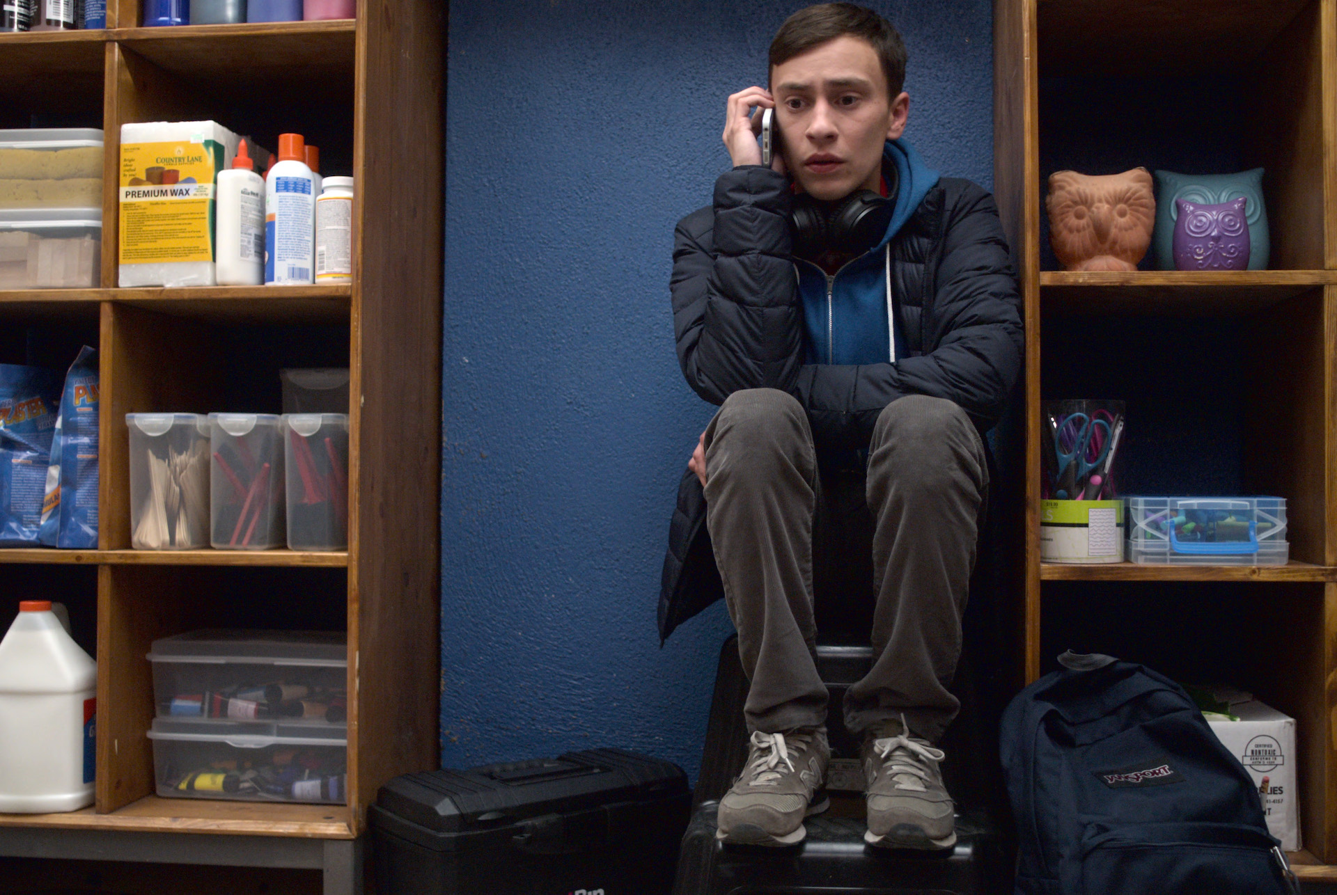 Sam Gardner (Keir Gilchrist) crouches between two shelving units on his phone in Aypical still - teen shows on Netflix
