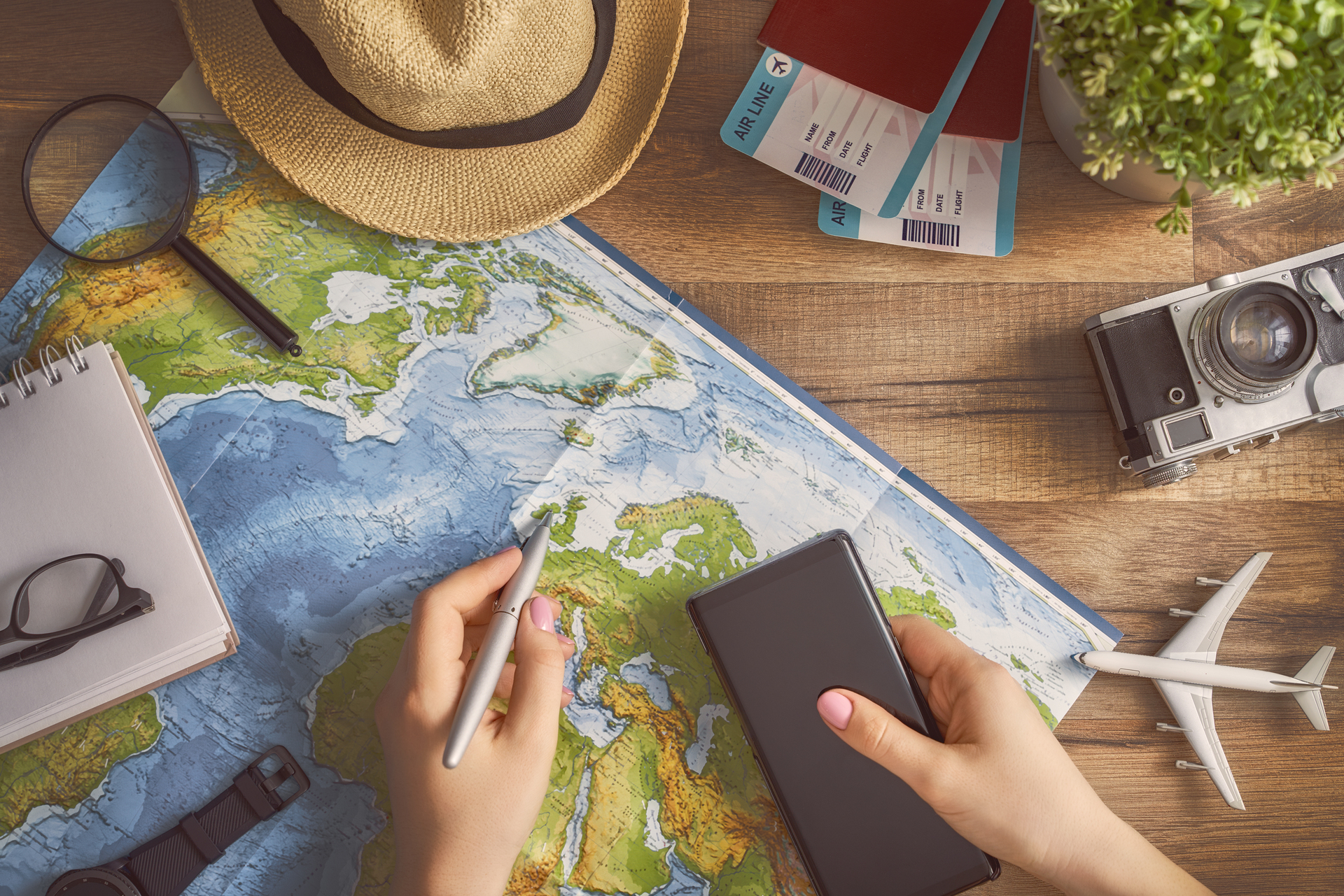 woman preparing for a journey with a map, pen, travel tickets, passport, hat, camera, and various other items.