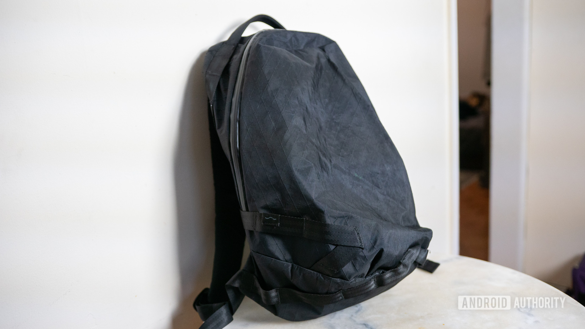 Black XPAC Able Carry Daily Backpack leaning against white wall