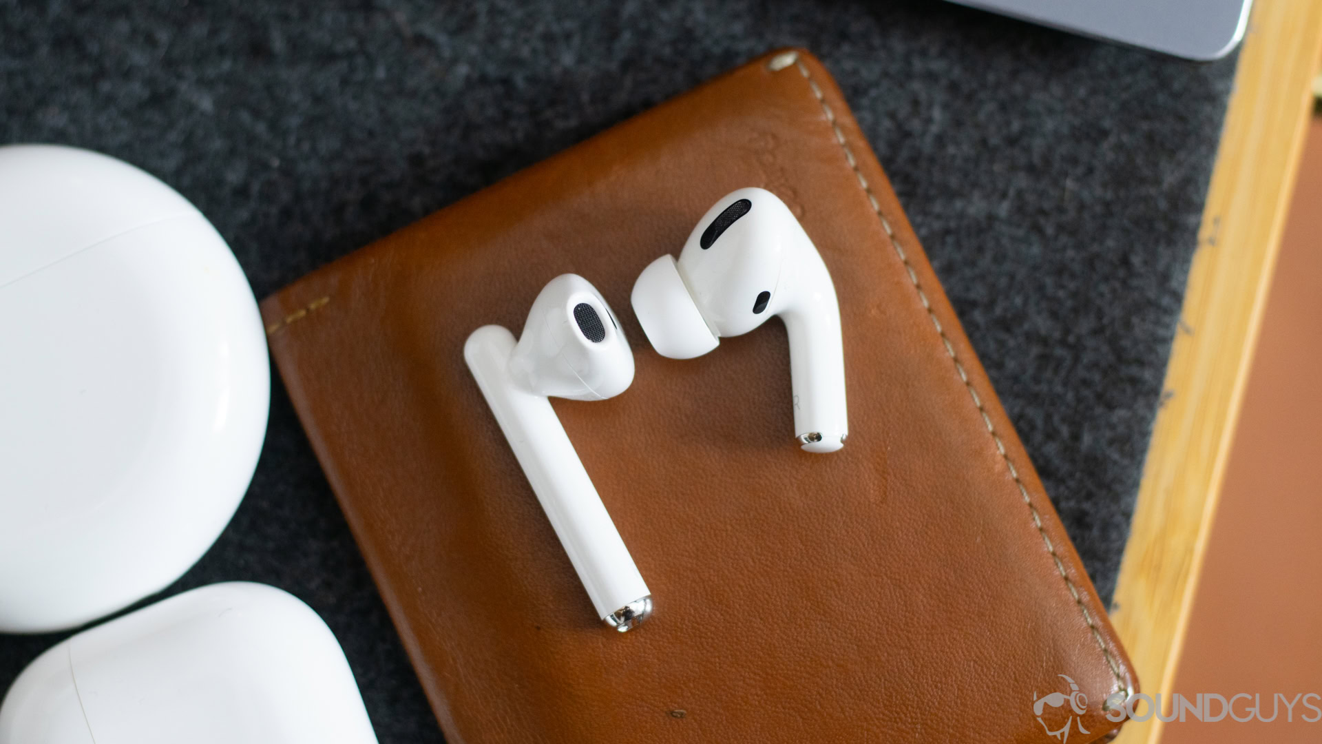 One single earbud of the AirPod Pro and Freebuds 3 side by side on a brown wallet