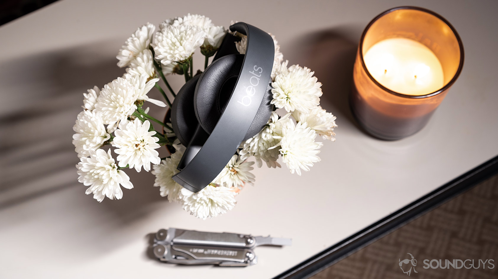 The Beats Solo3 Wirless headphones folded atop a bed of flowers with a candle and multitool.