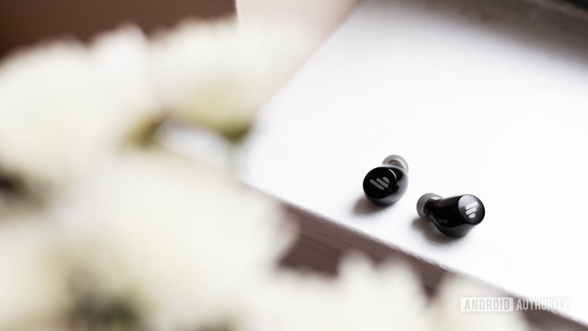 A picture of the Edifier TWS1 true wireless earbuds on a windowsill with flowers in the foreground.