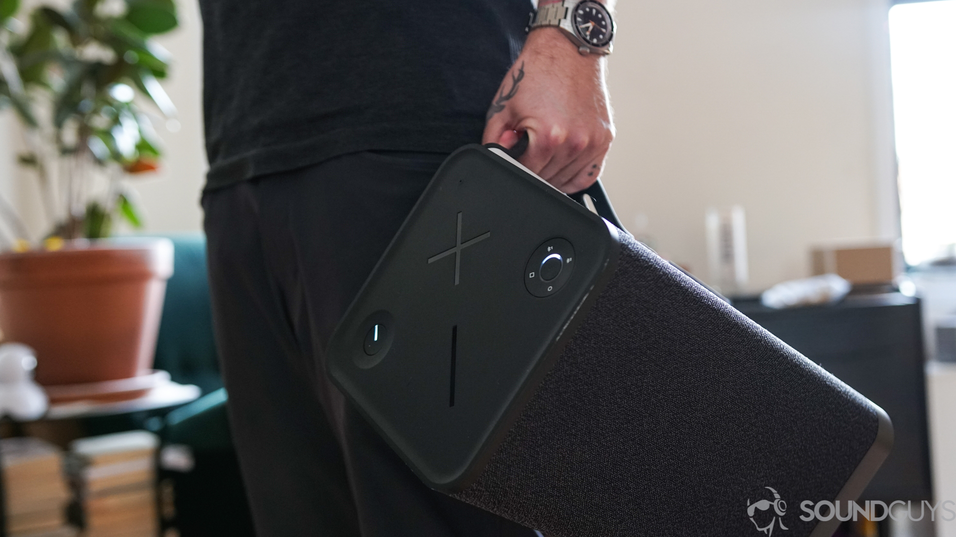 A man carries the UE Hyperboom portable bluetooth speaker across a living room.