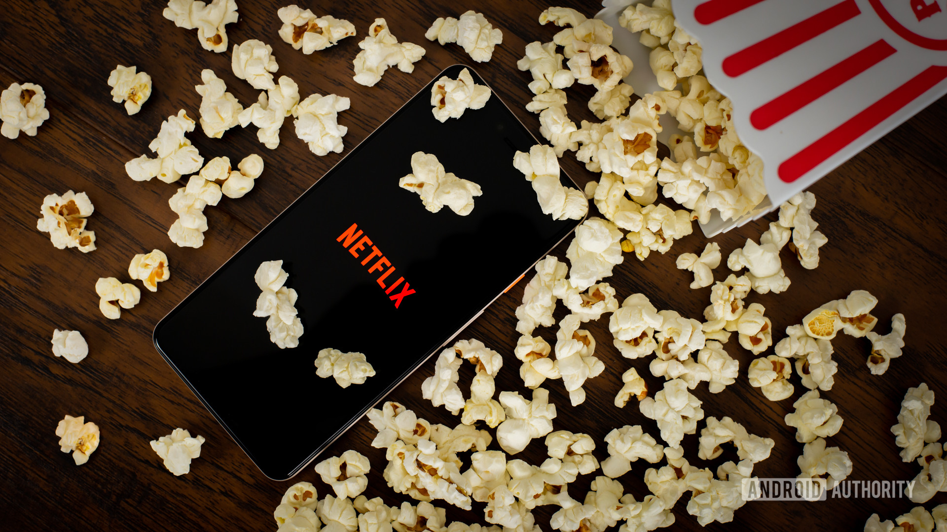 Netflix logo on a phone screen next to a spilled container of popcorn.
