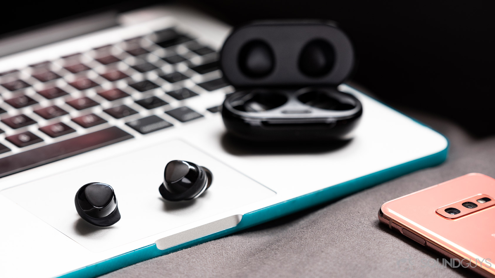 A picture of the Samsung Galaxy Buds Plus true wireless earbuds outside of the open charging case atop a Macbook Pro.