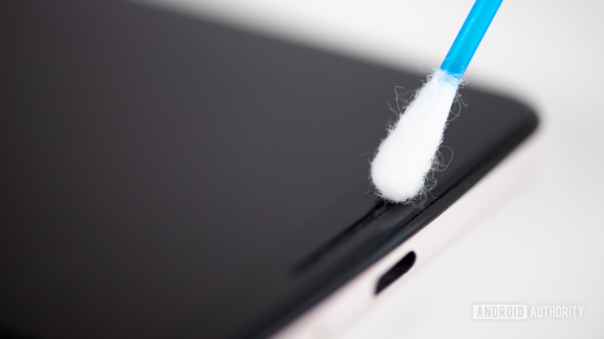 A photo of a cotton swab cleaning a phone.