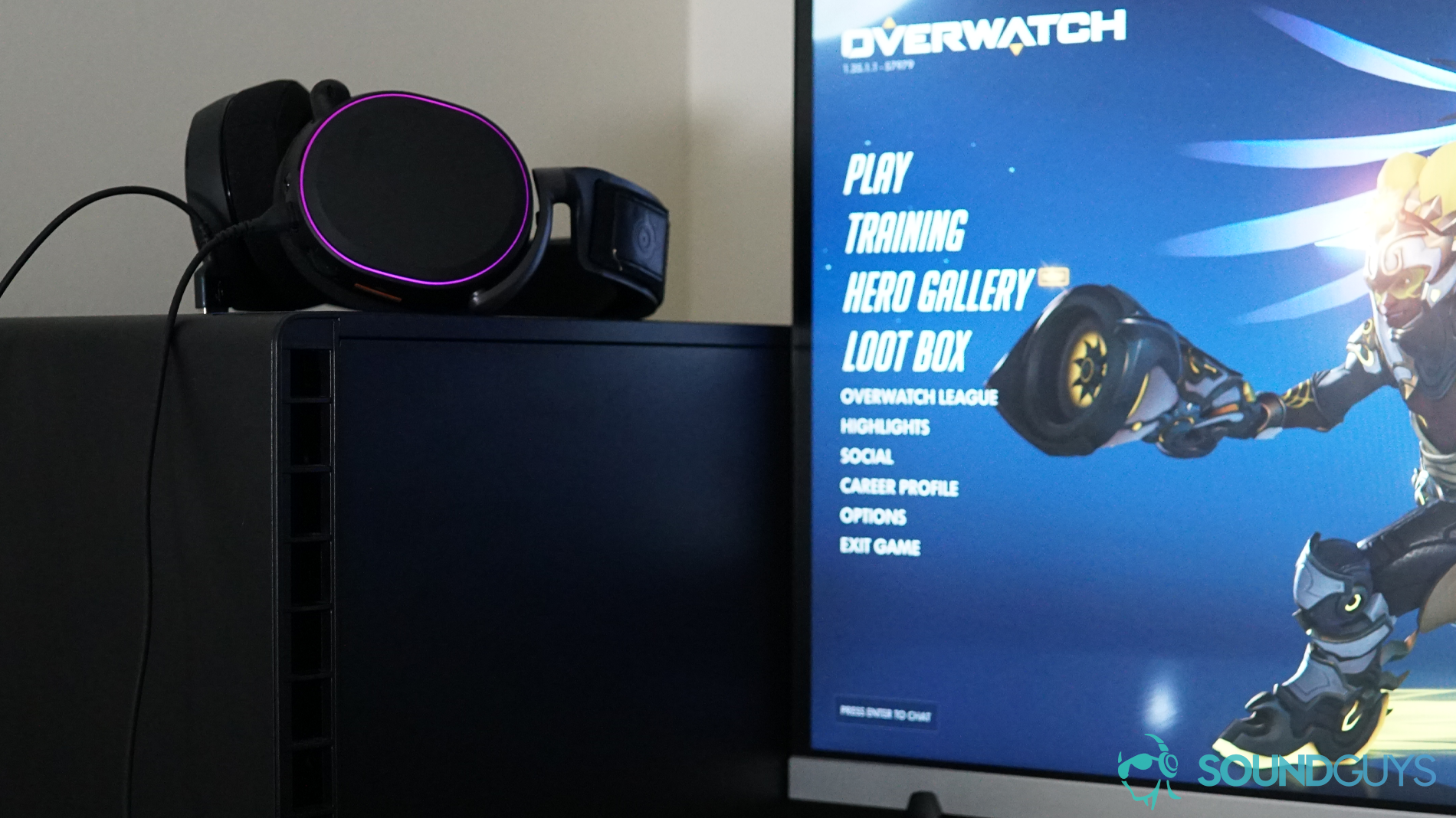 The SteelSeries Arctis Pro sits on a desktop PC tower next to a monitor with Overwatch running.