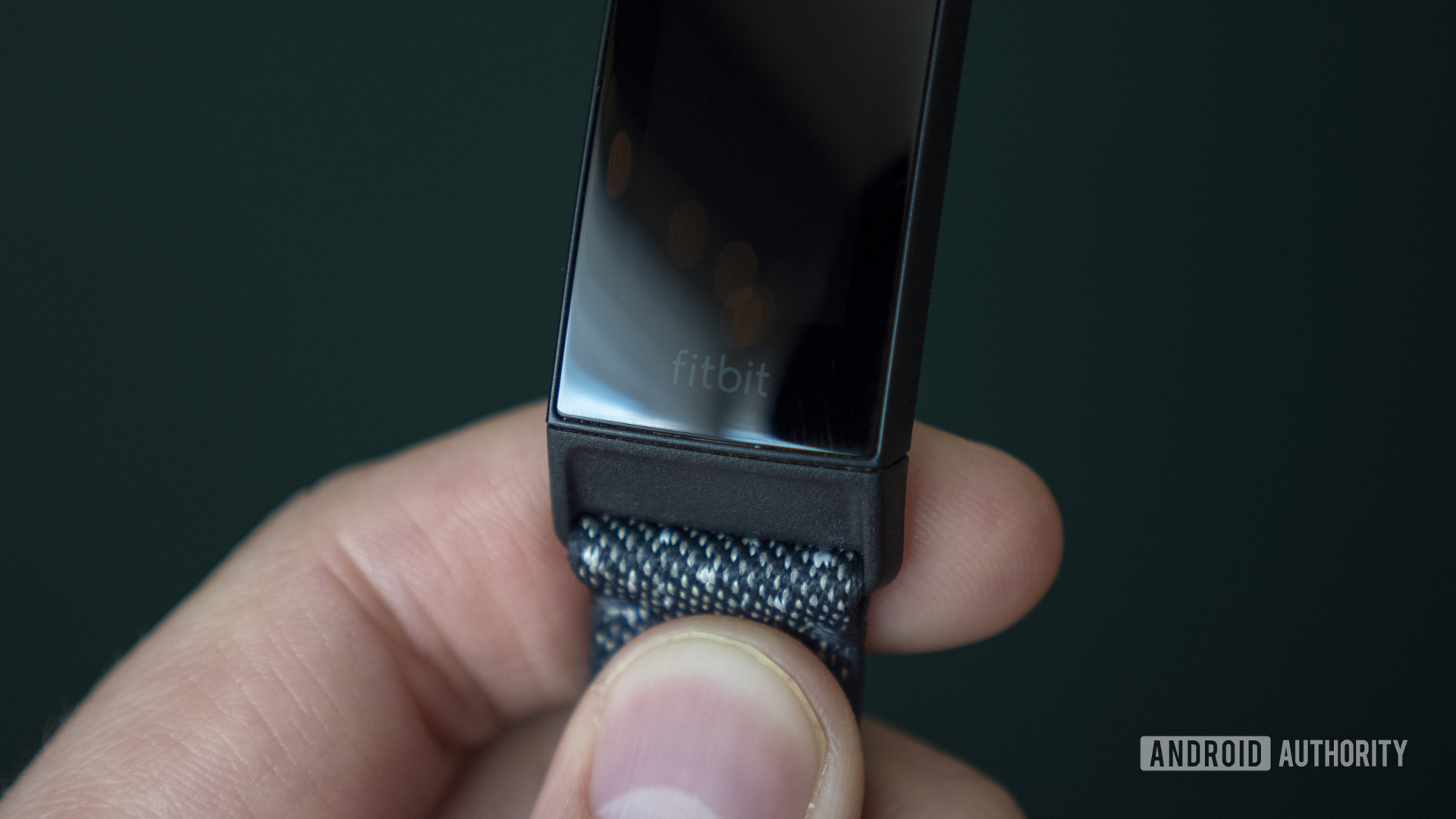 A user holds a Fitbit Charge 4 in hand.