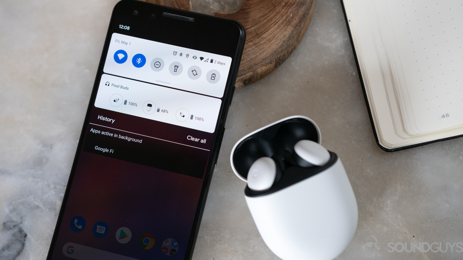 The Google Pixel Buds 2020 true wireless earbuds case is opened and next to the Pixel smartphone with the Bluetooth drop-down menu displayed.