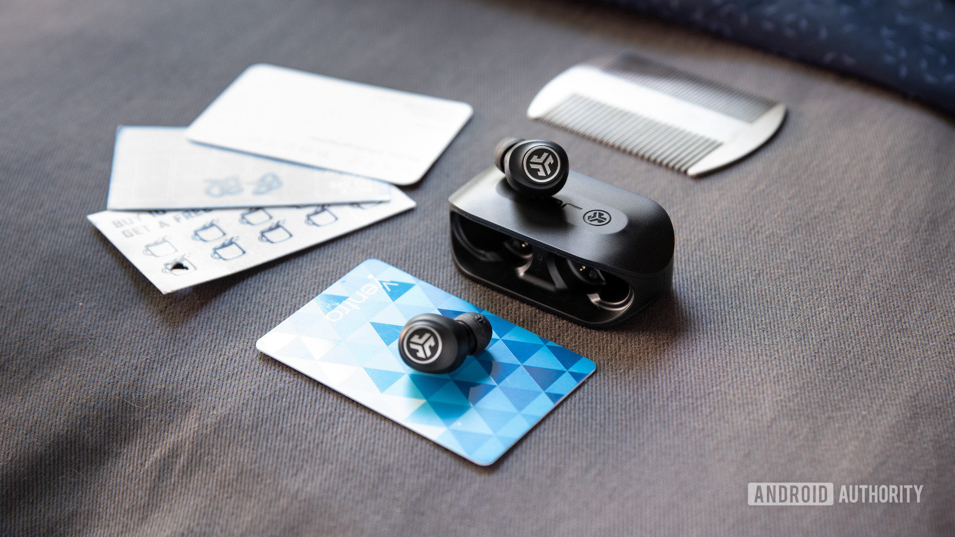 The JLab GO Air cheap true wireless earbuds sitting atop the charging case; punch cards are nearby for a size comparison.