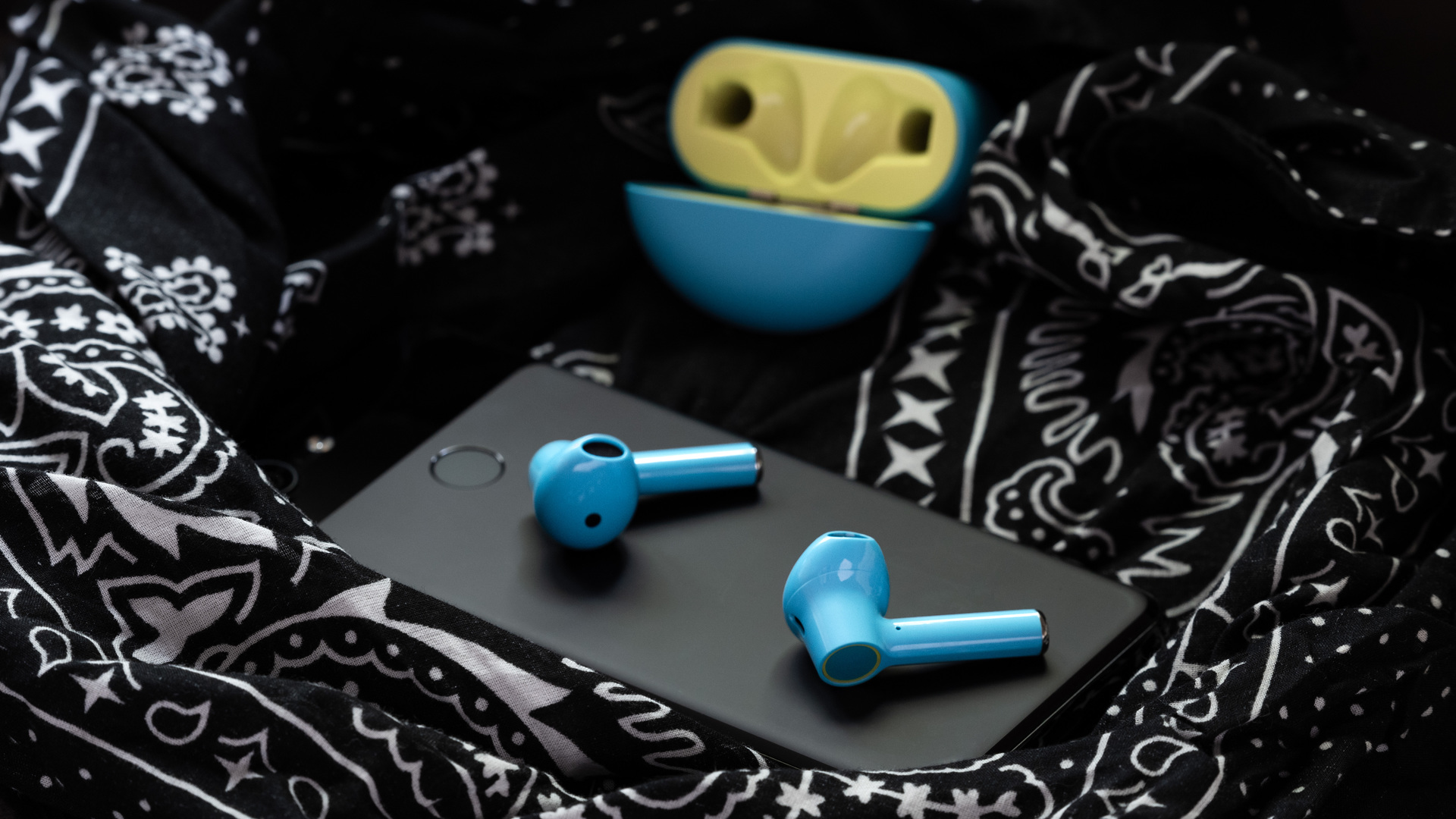 A picture of the OnePlus Buds true wireless earbuds (Nord Blue color) on a Google Pixel 3 smartphone with the earbuds charging case open in the background.
