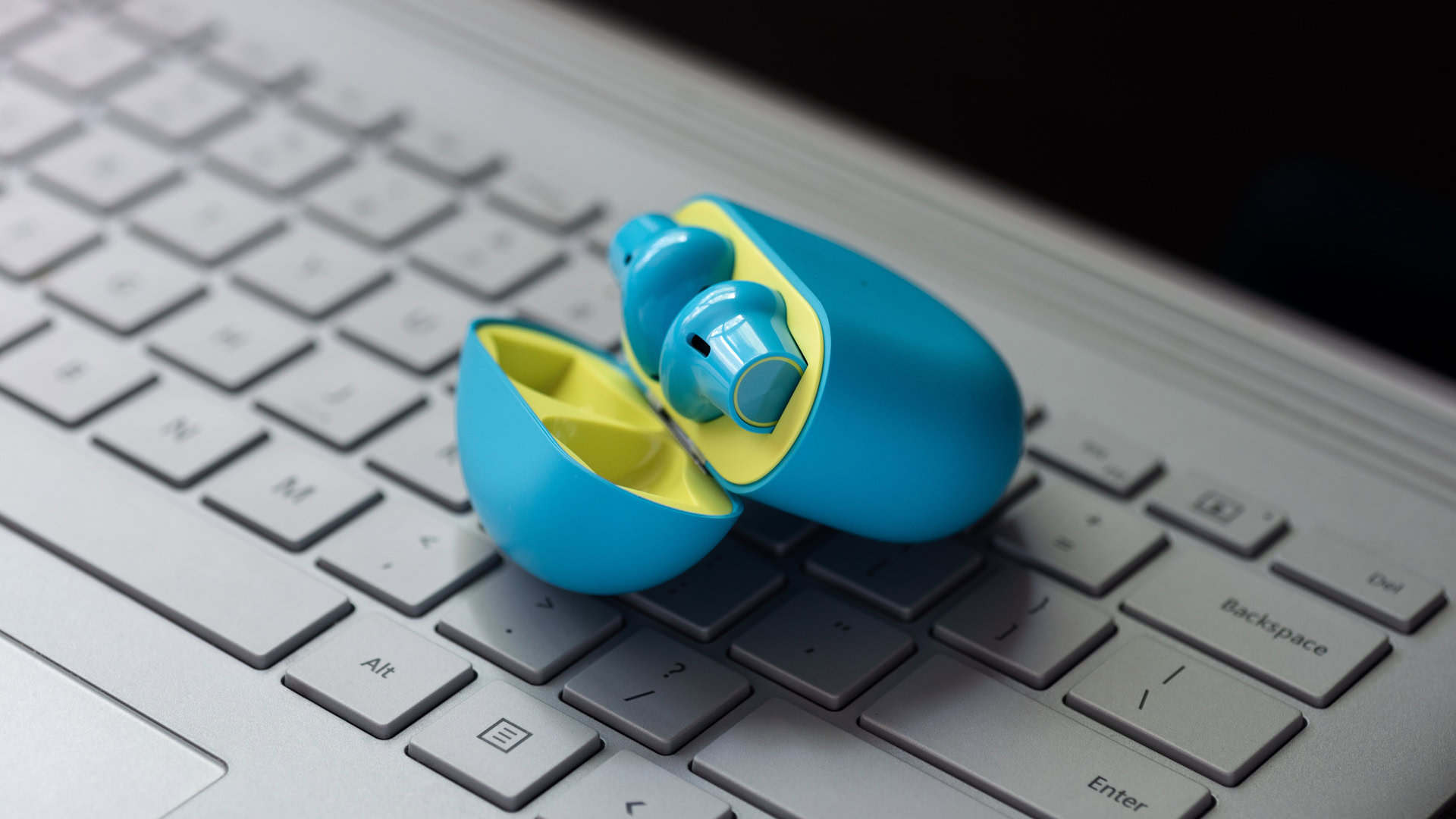 A picture of the OnePlus Buds true wireless earbuds in the open charging case atop a Microsoft Surface Book laptop.