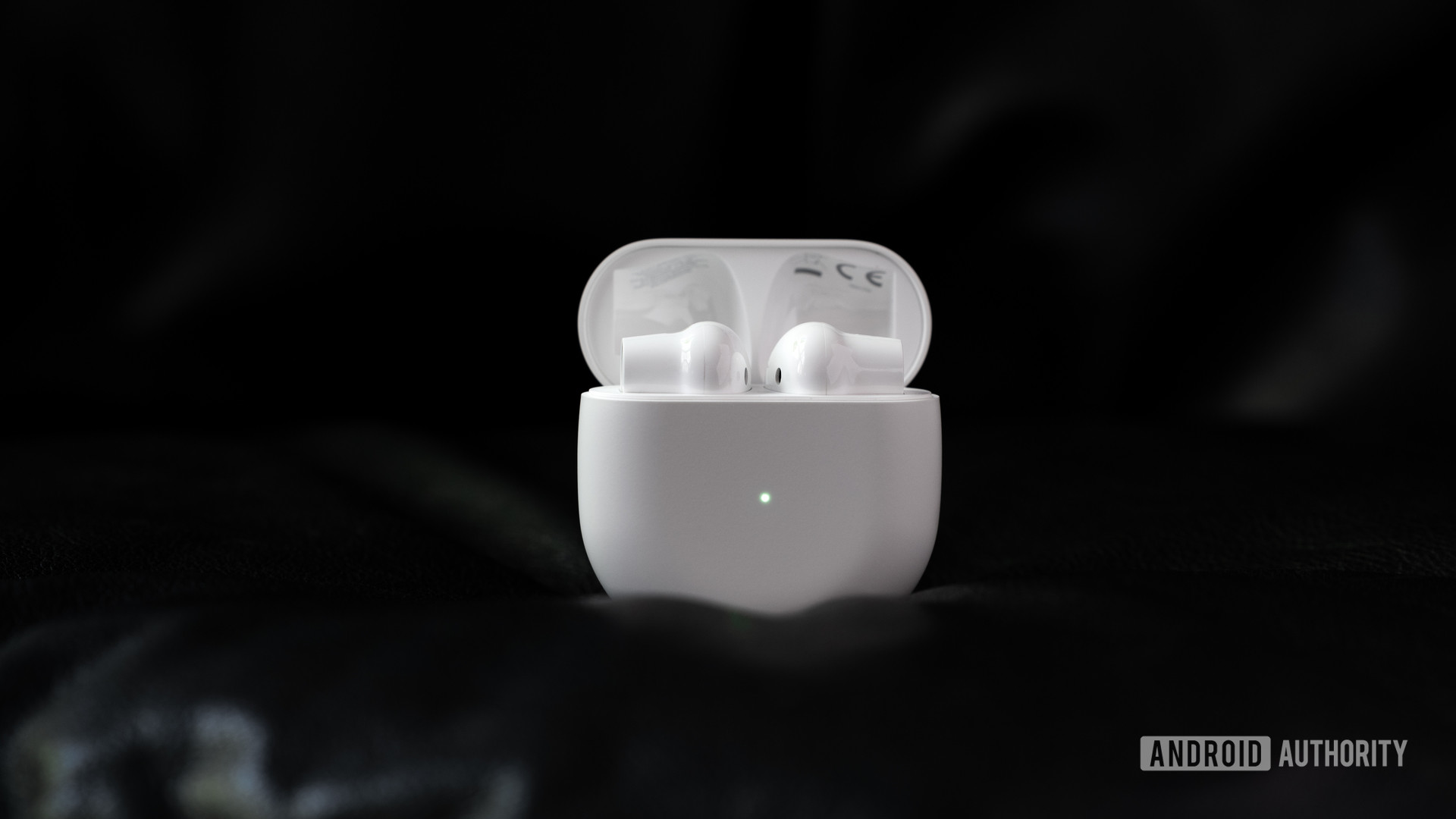 A picture of the OnePlus Buds true wireless earbuds (white) in the open charging case, which is standing erect against a black background.