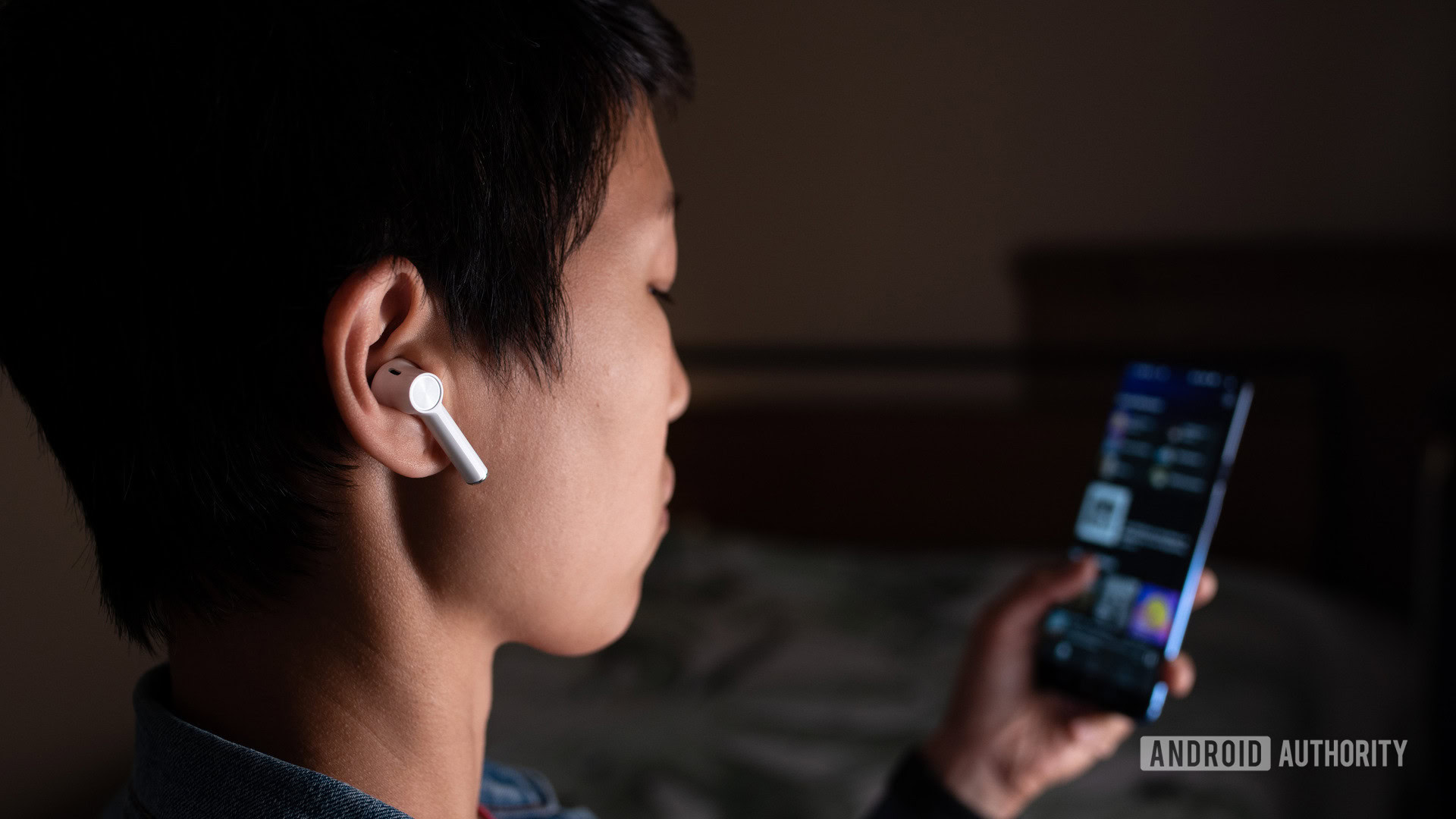 A picture of the OnePlus Buds true wireless earbuds (white) being worn by a woman looking at Spotify on the OnePlus 7 smartphone.