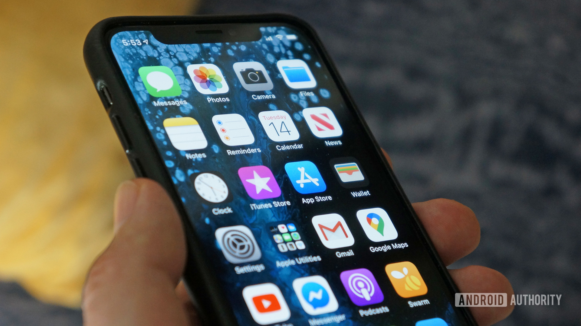 An Apple iPhone XS being held by a hand with its screen on showing various app icons.