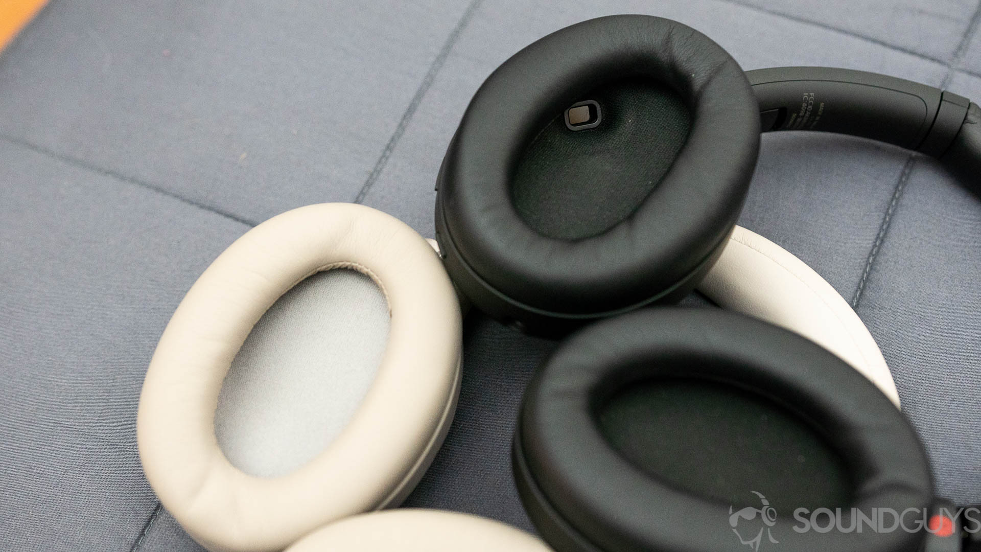 The Sony WH-1000XM3 and Sony WH-1000XM4 lay on on top of the other, with their ear cups facing up, showing the interior sensor on the WH-1000XM4.