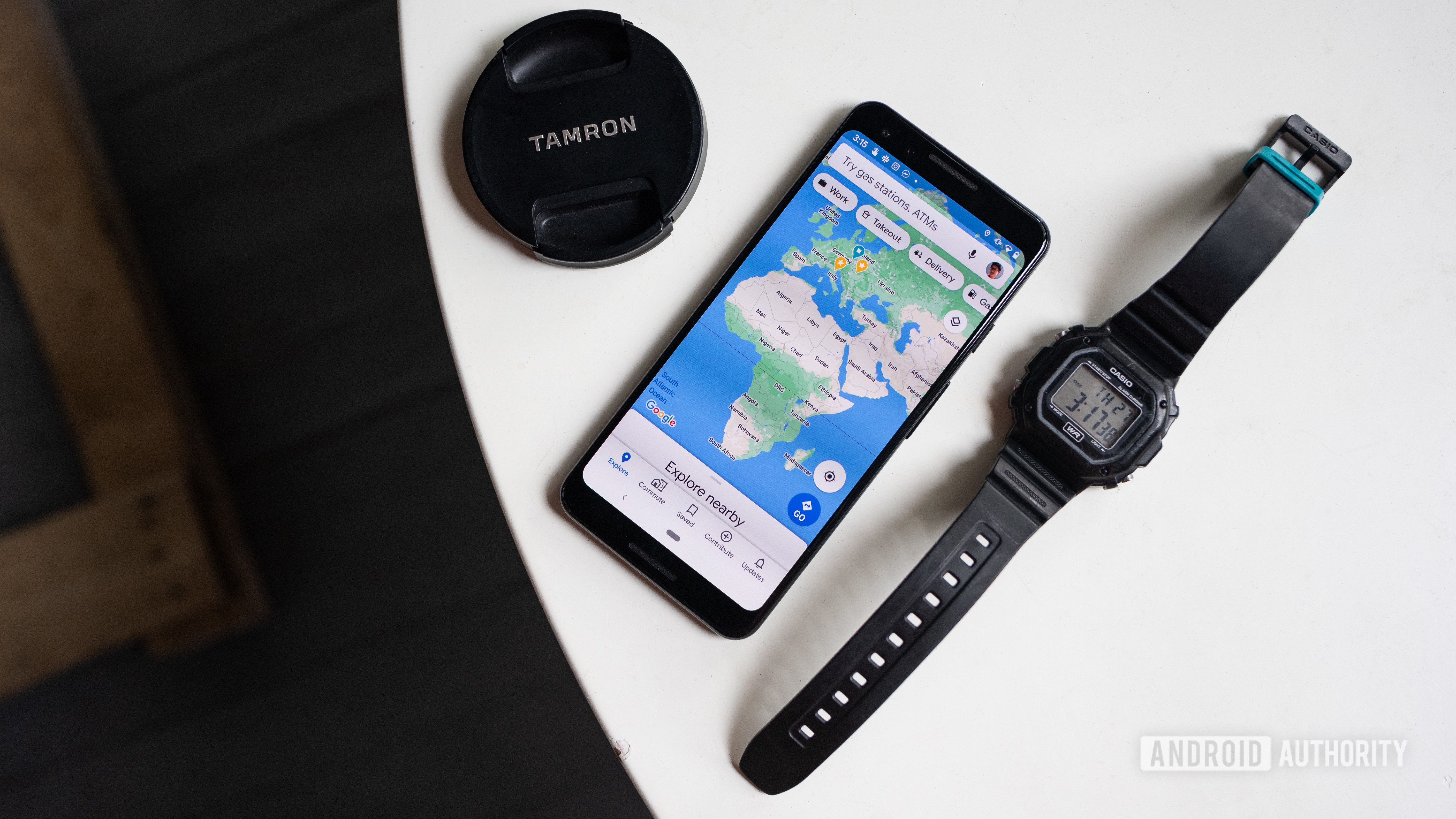 An aerial photo of the Google Maps app open on a Google Pixel 3 smartphone, which is flanked by a Tamron lens cap and Casio watch on a white table.