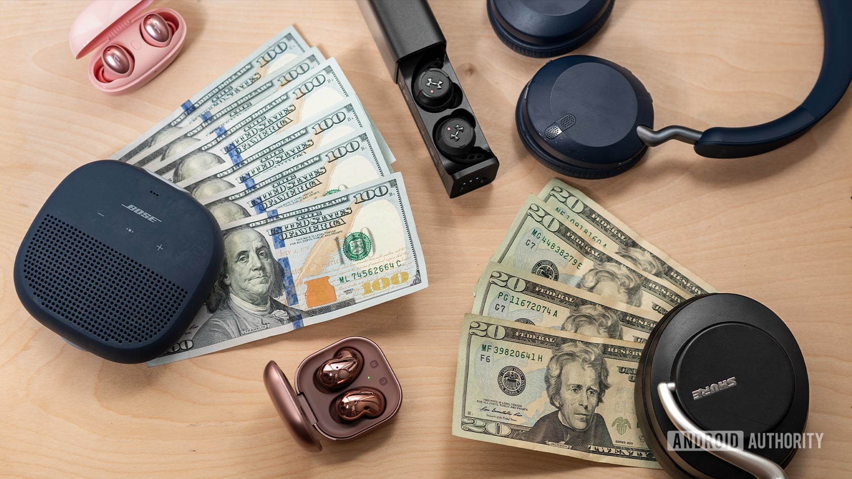 An image of money surrounded by wireless audio products like the Bose SoundLink Micro speaker, Samsung Galaxy Buds Live, 1MORE Colorbuds, Jabra Elite 45h, JBL True Wireless Flash X, and Shure AONIC 50.