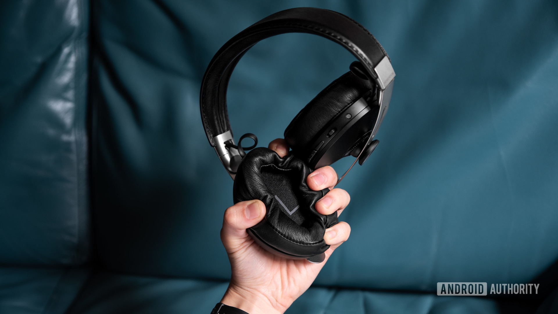 A hand holds the Sennheiser Momentum Wireless 3 Bluetooth headphones by the ear pads, and squeezes them.