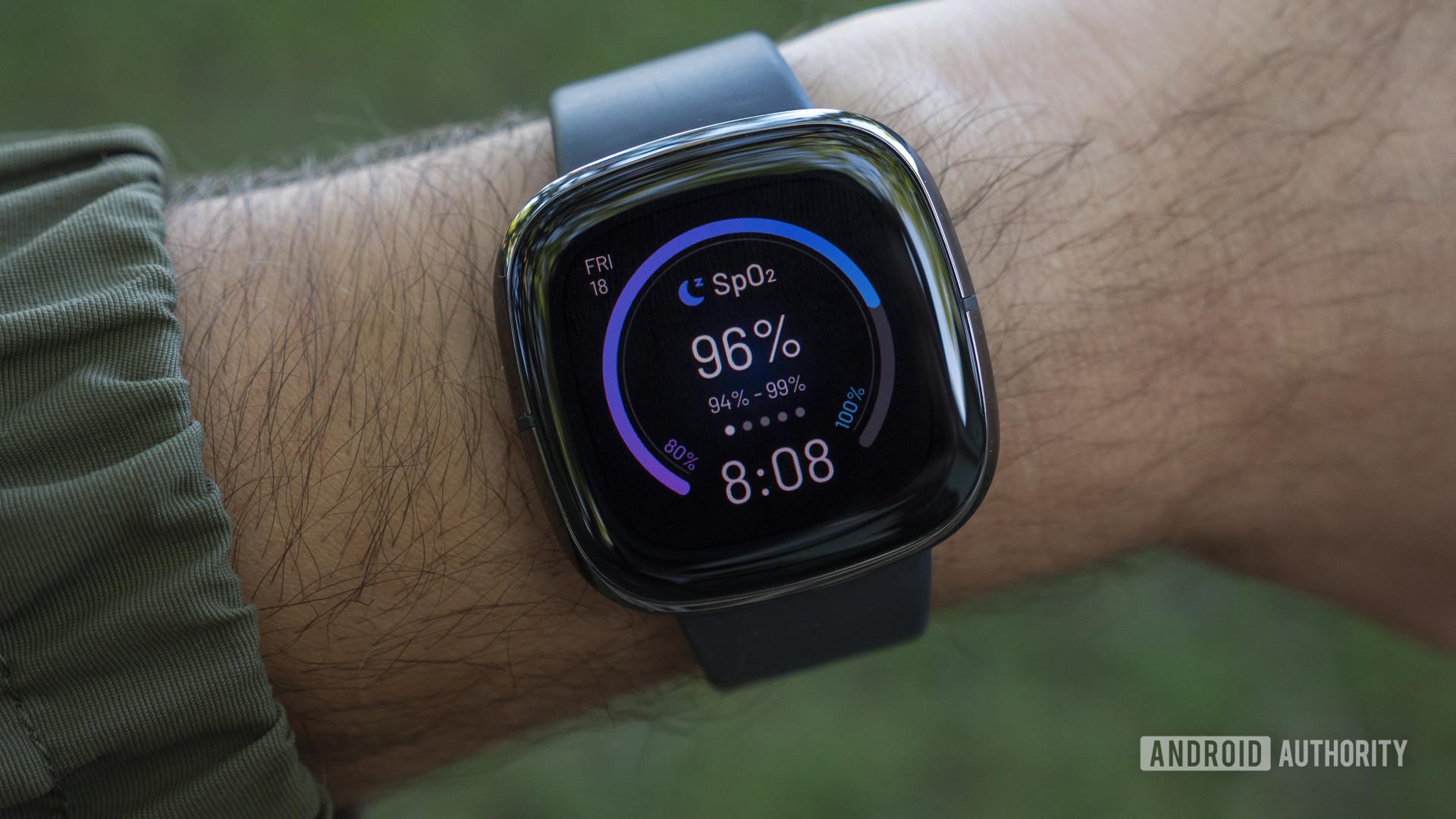 A Fitbit Sense on a man's wrist displays a watch face loaded with health stats.