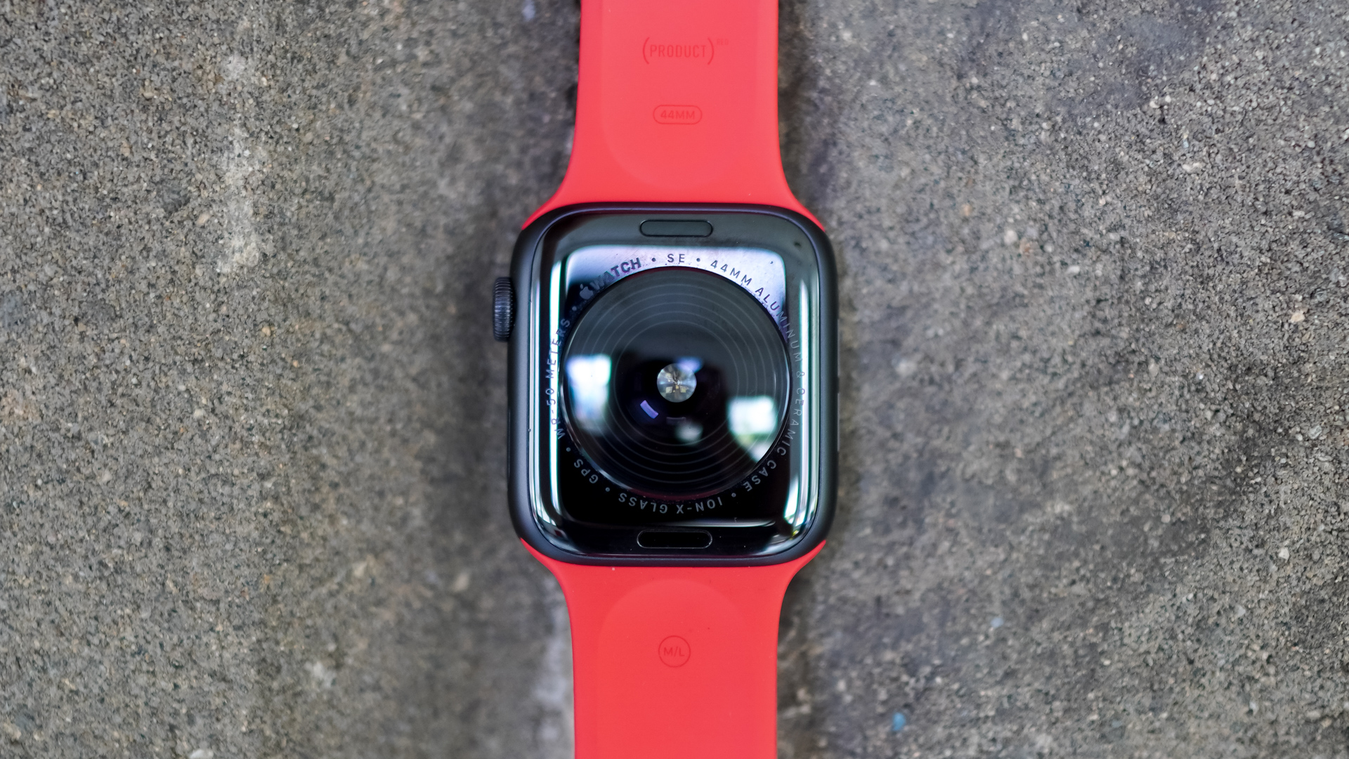 An Apple Watch SE rests face down on a stone surface showing the sensors on the back of the device.