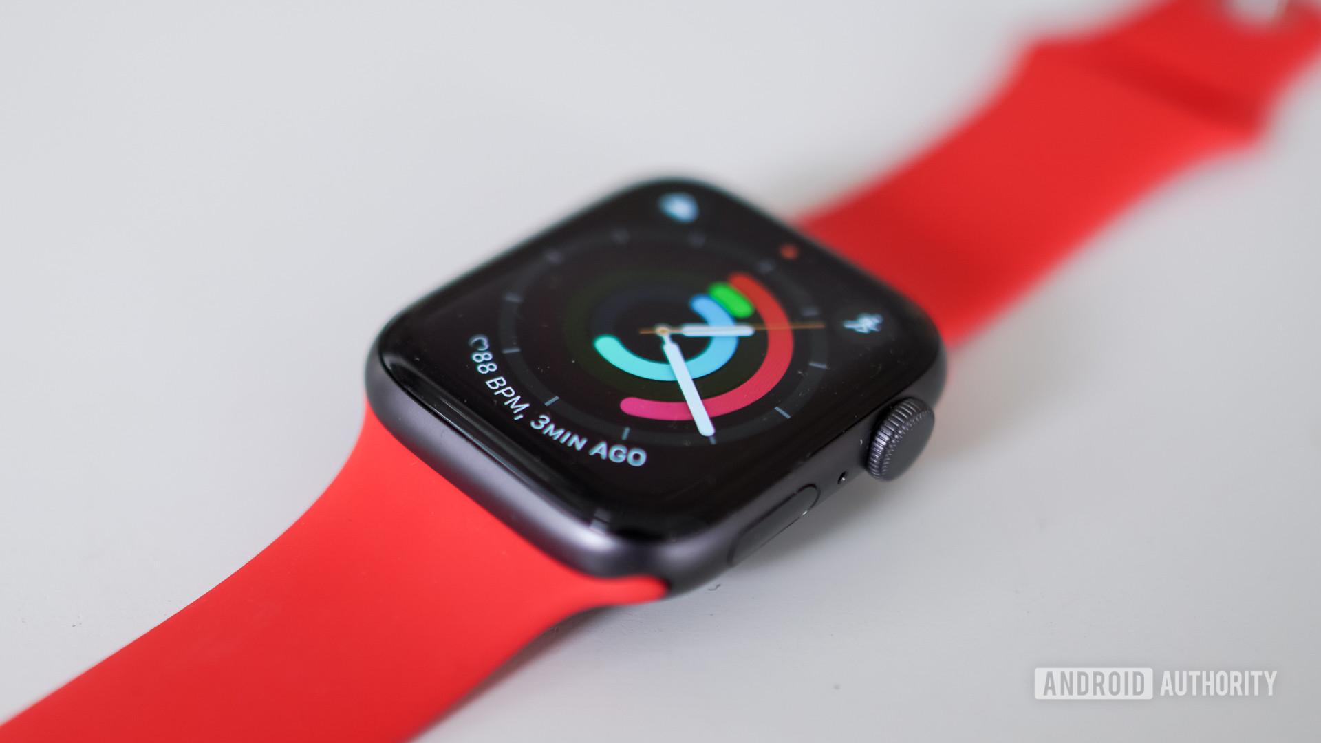 An Apple Watch SE in Space Gray with a a red band rests on a white table.