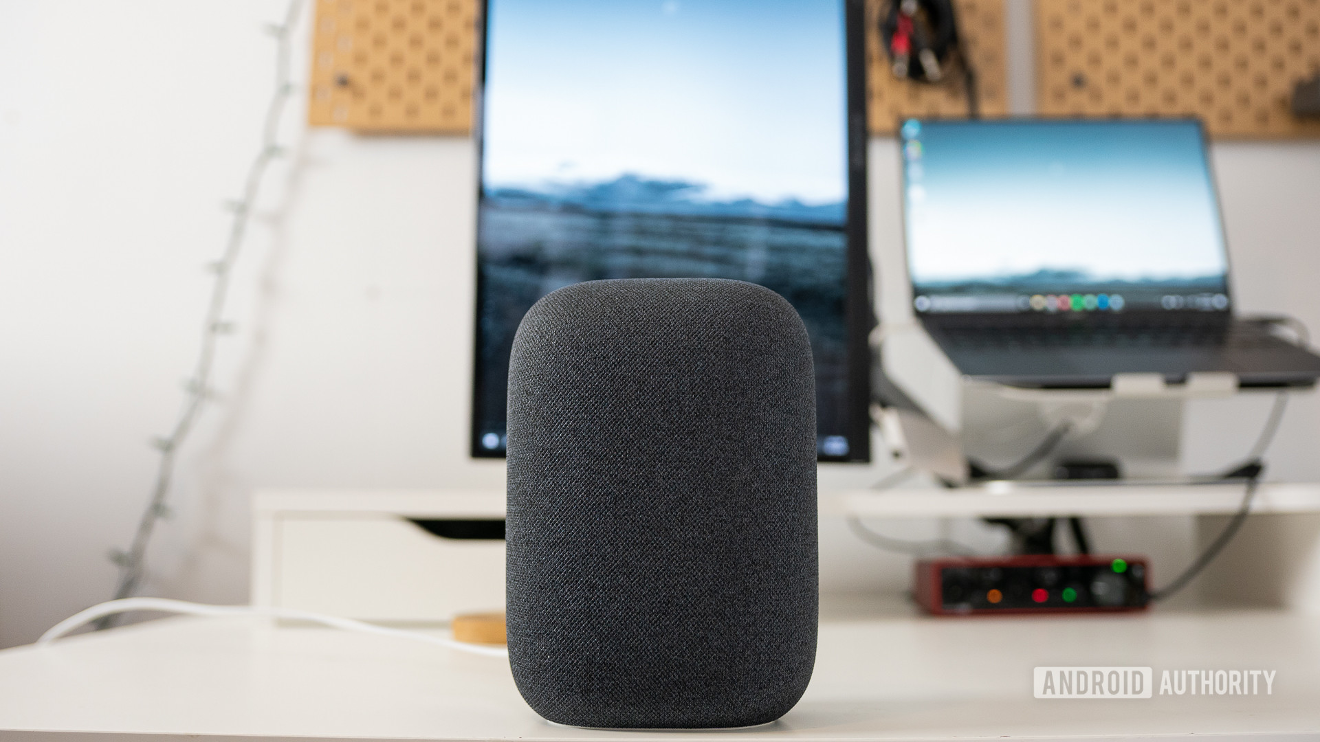 The gray Google Nest Audio speaker pictured on a white desk in front of computer screens. Headphone volume booster