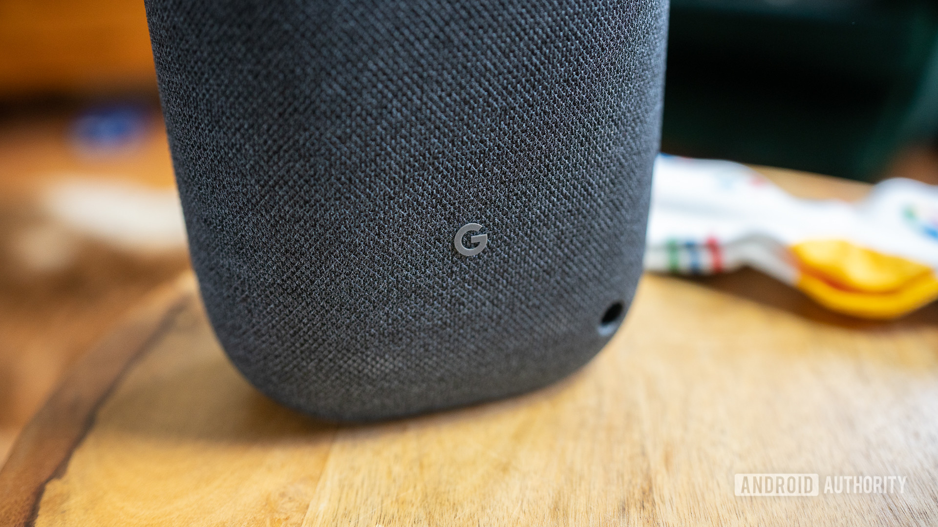 Pictured is the &quot;G&quot; logo on the back on the Google Nest Audio on a wooden surface