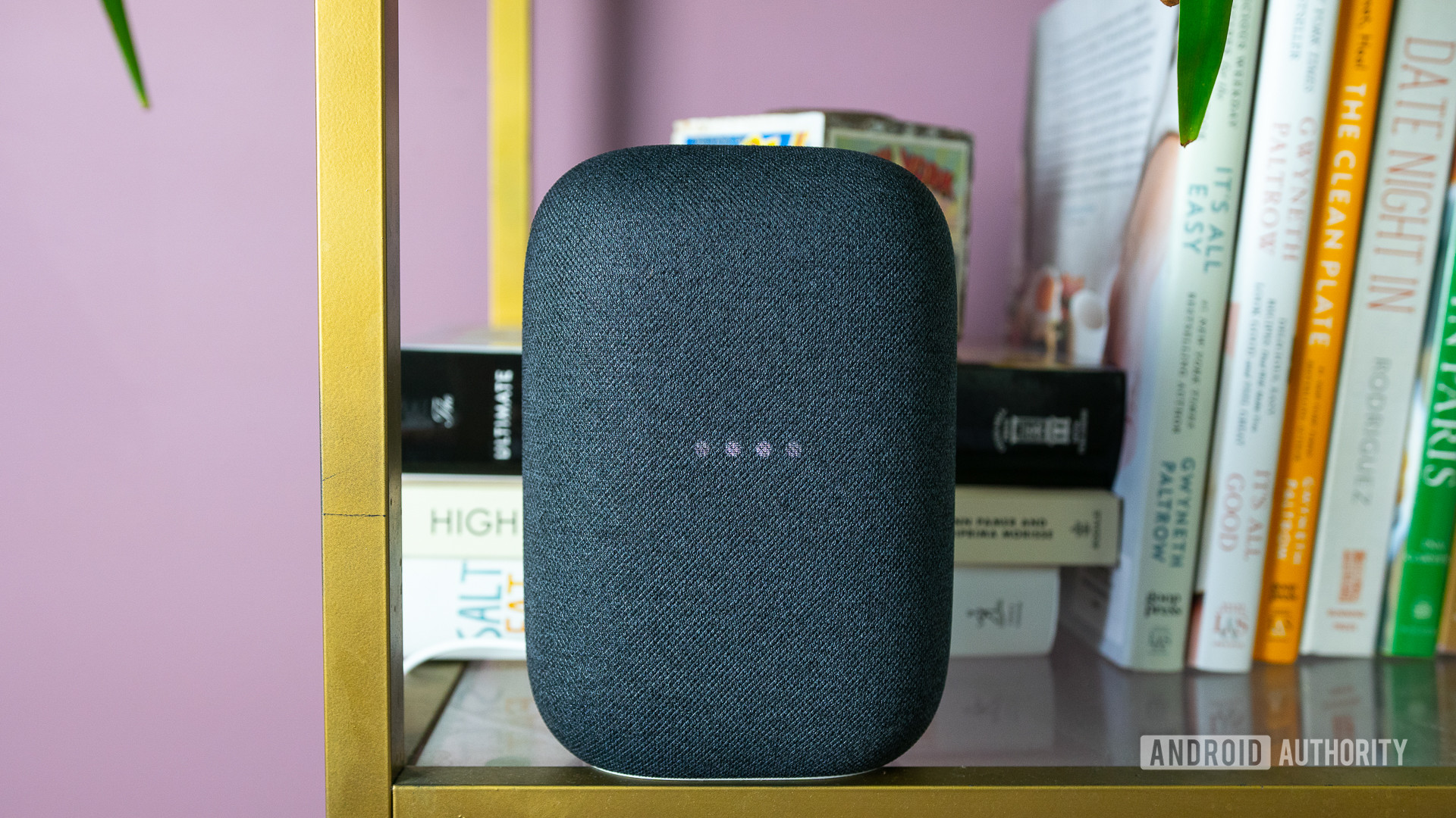 The gray Google Nest Audio on a bookshelf with the lights blinking.