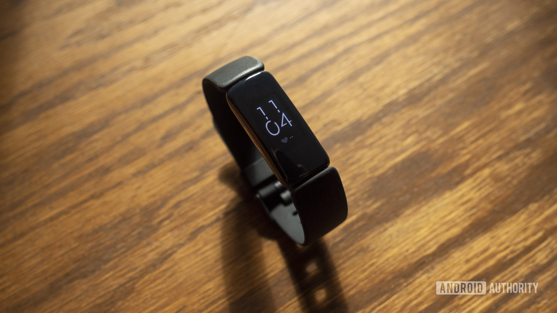 A Fitbit Inspire 2 rests on a wooden table displaying a clock face.