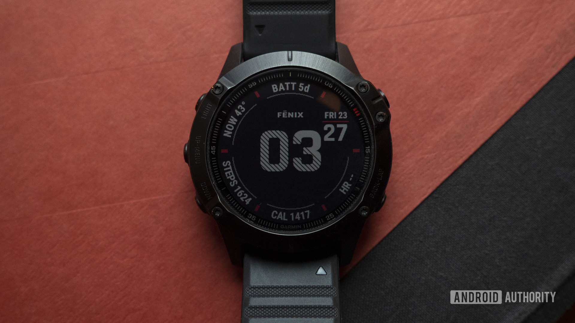 A Garmin Fenix 6 Pro rests on a red and black book displaying the watch face.