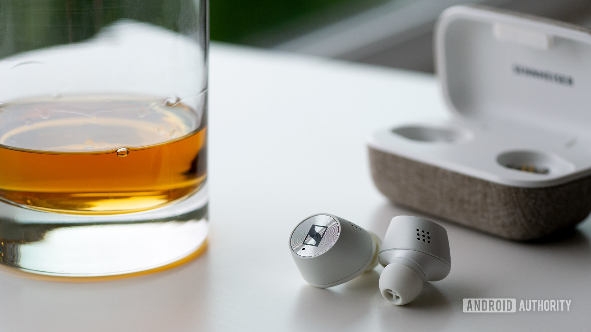 The Sennheiser momentum true wireless 2 noise-cancelling earbuds next to a glass of whiskey.