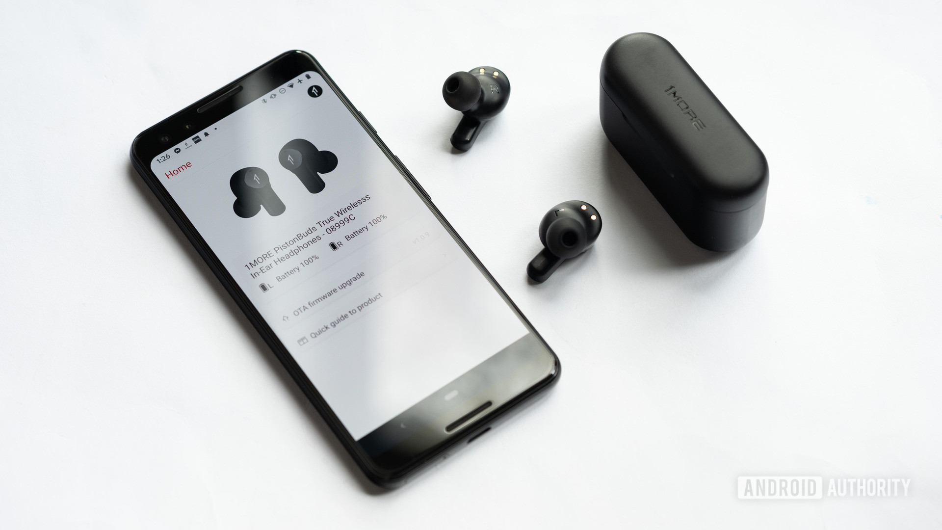 The 1MORE PistonBuds cheap true wireless earbuds outside of the closed charging case, and next to a Google Pixel 3 smartphone with the 1MORE Music app open.
