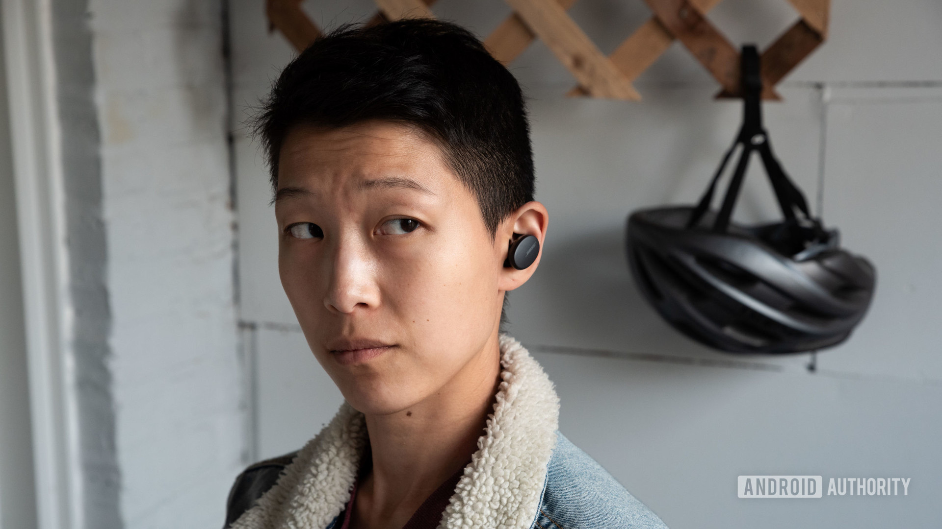 A woman wears the Bose Sport Earbuds true wireless workout earbuds with a biking helmet in the background.