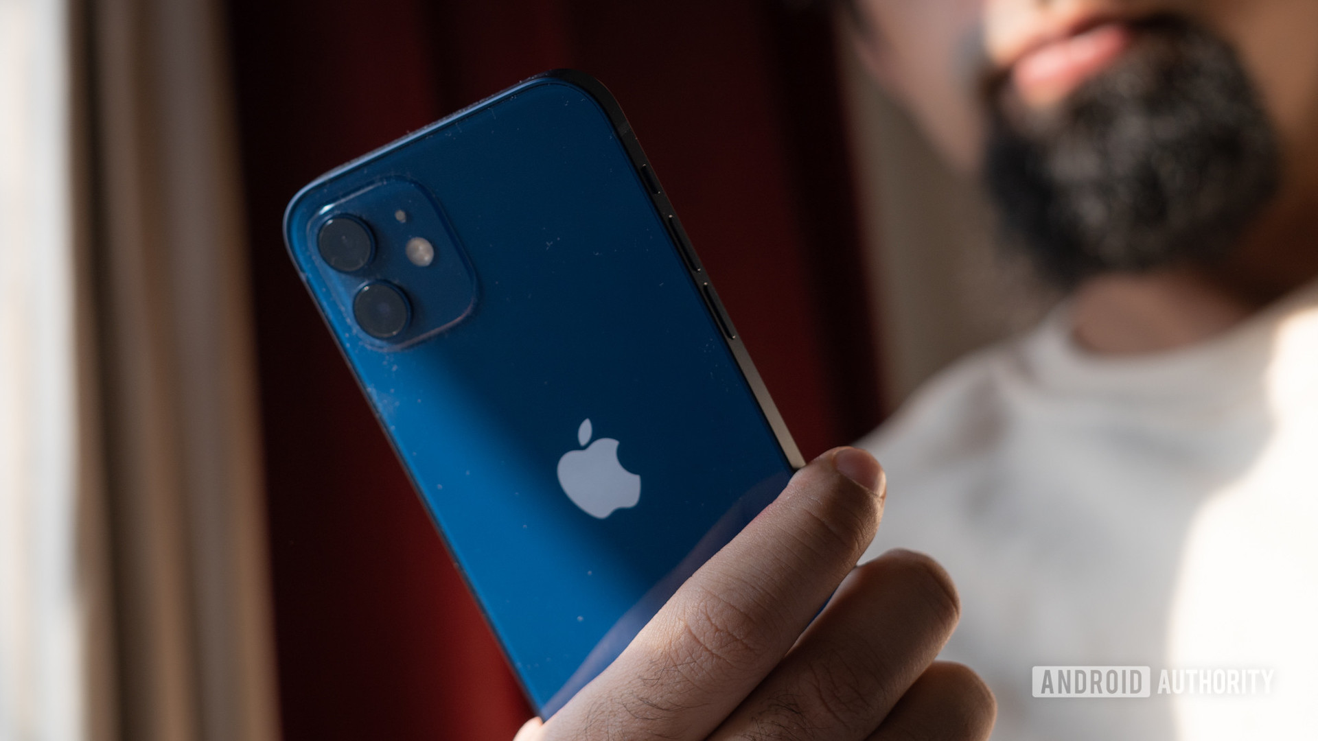 A man holding an iPhone 12 in hand, showing the rear of the older phone with camera and Apple logo