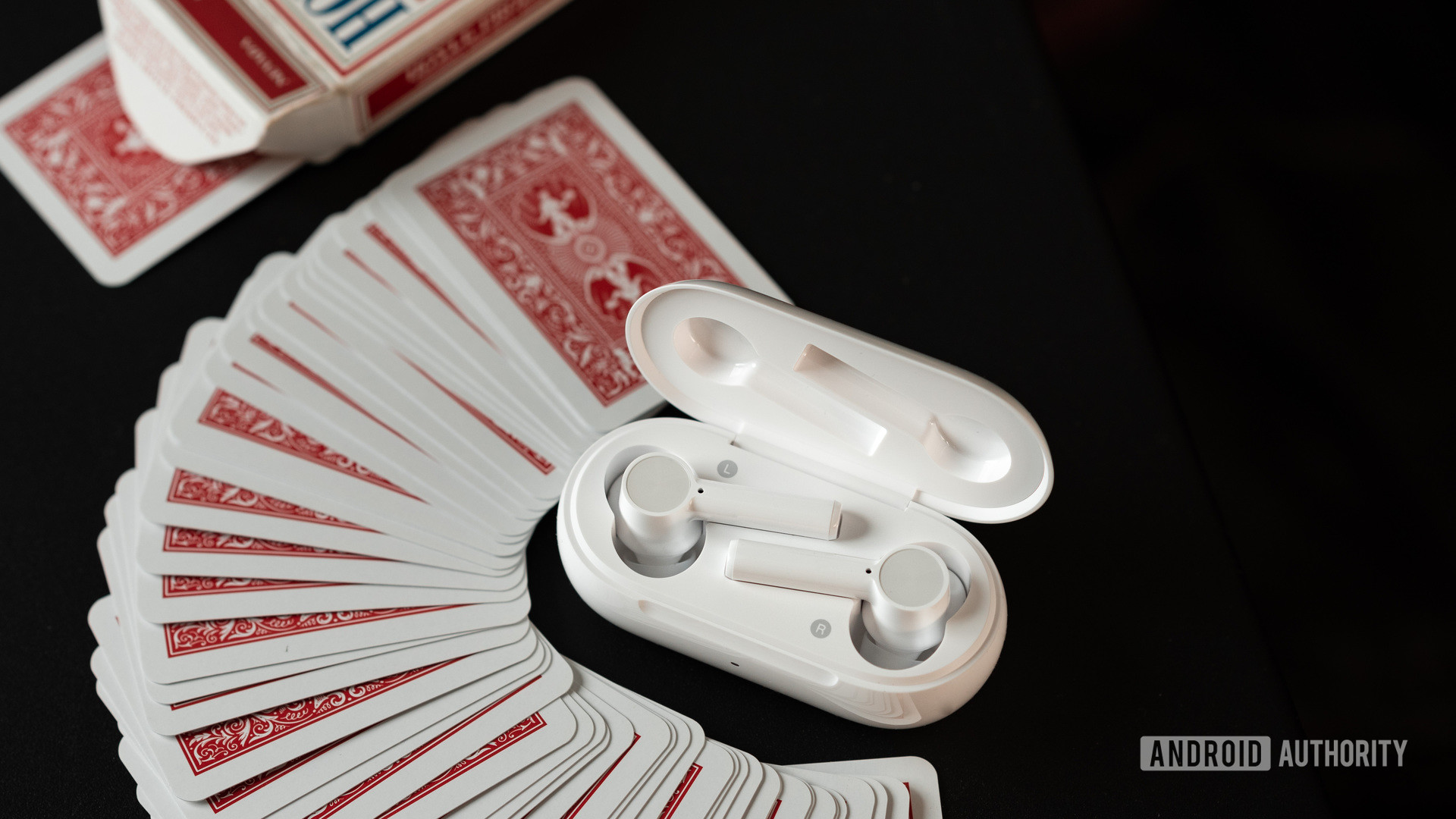 The OnePlus Buds Z cheap true wireless earbuds in white rest in the charging case which is surrounded by a pile of mini red playing cards.