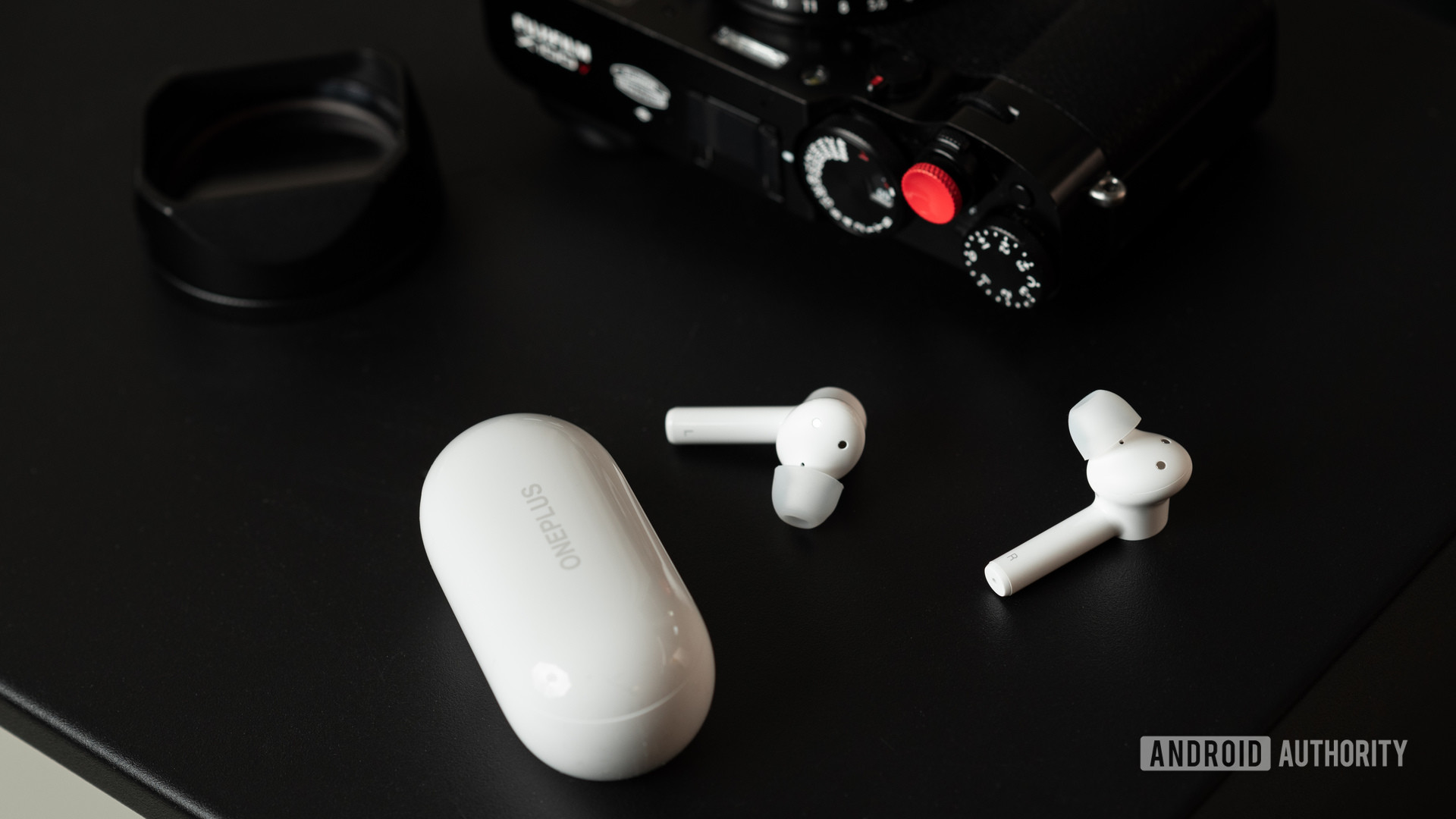 The OnePlus Buds Z cheap true wireless earbuds on a table next to a camera and the charging case.