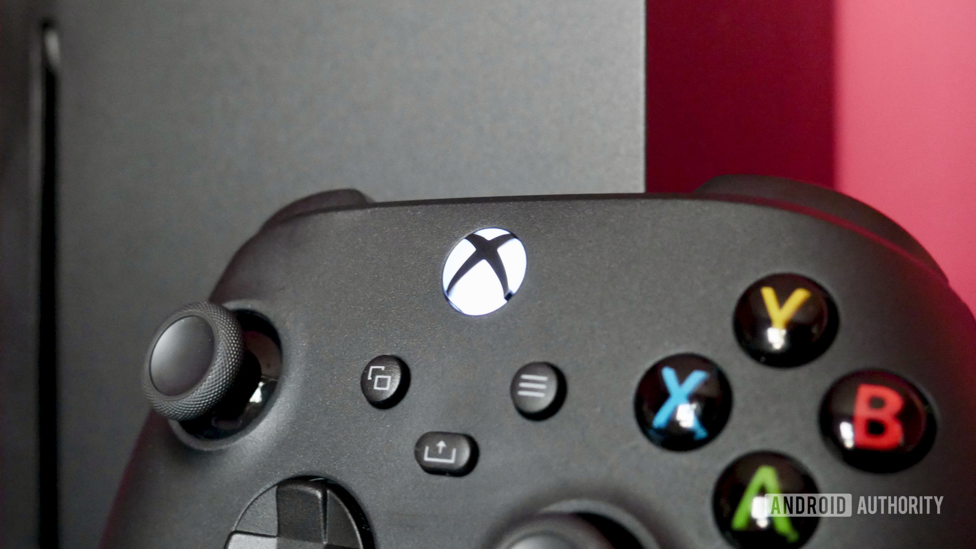 An Xbox Series X review controller lying against the console and a red wall.