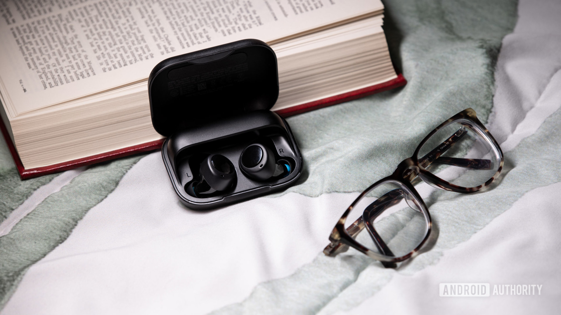 The Amazon Echo Buds true wireless earbuds in the charging case next to a pair of glasses.