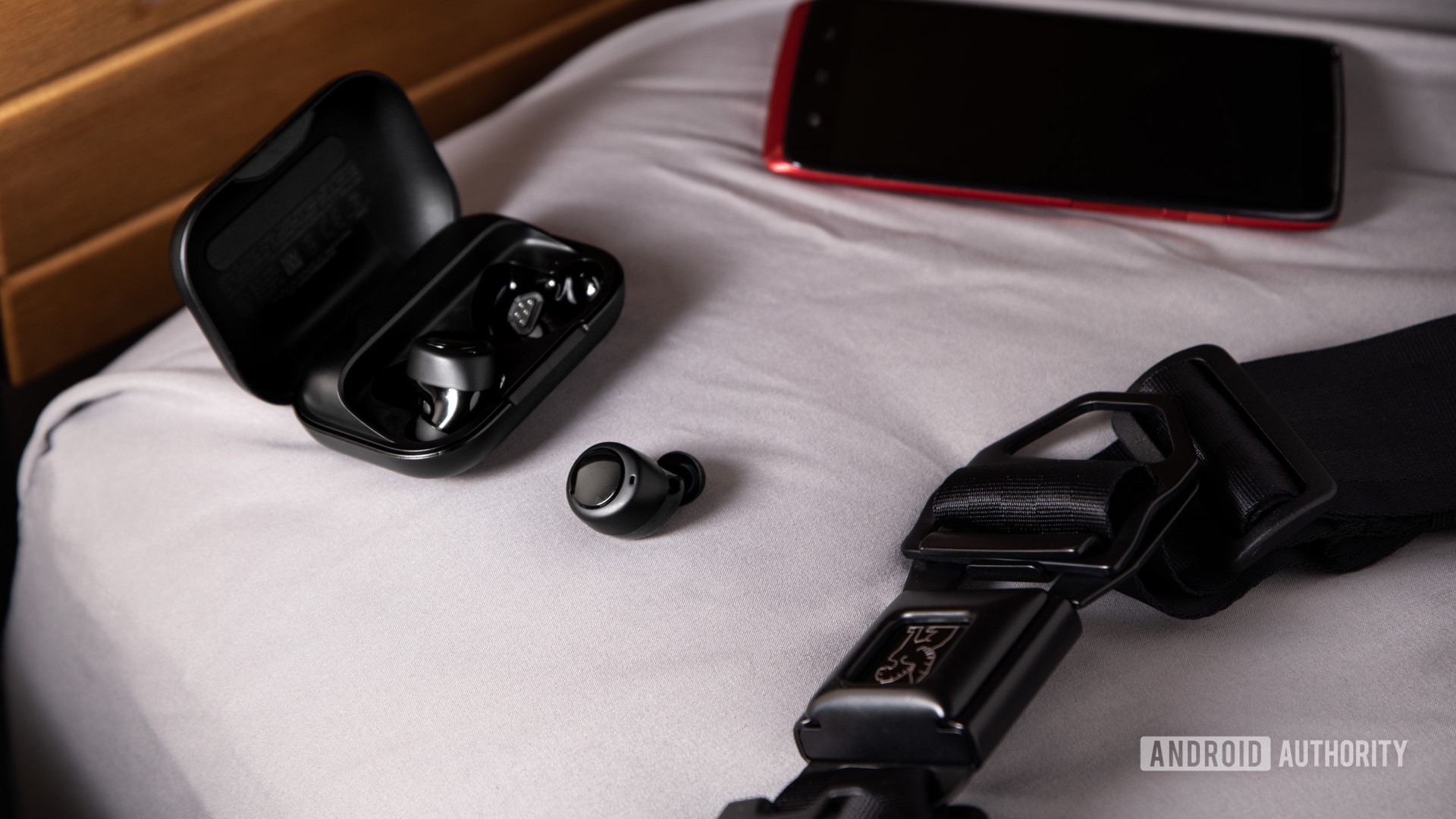 The Amazon Echo Buds true wireless earbuds outside of the open charging case next to a red smartphone.