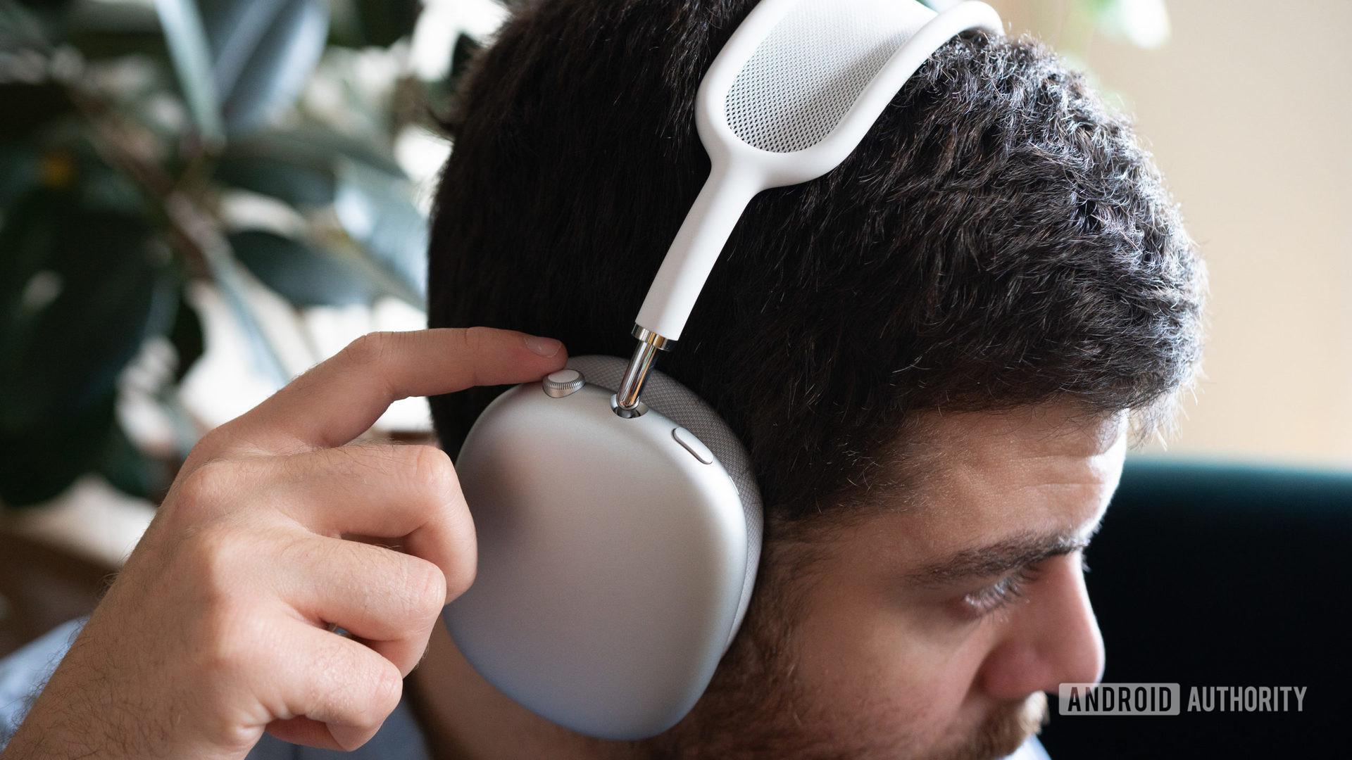 Bir adam Apple AirPods Max takıyor ve yerleşik kulaklık kontrollerini kullanıyor.