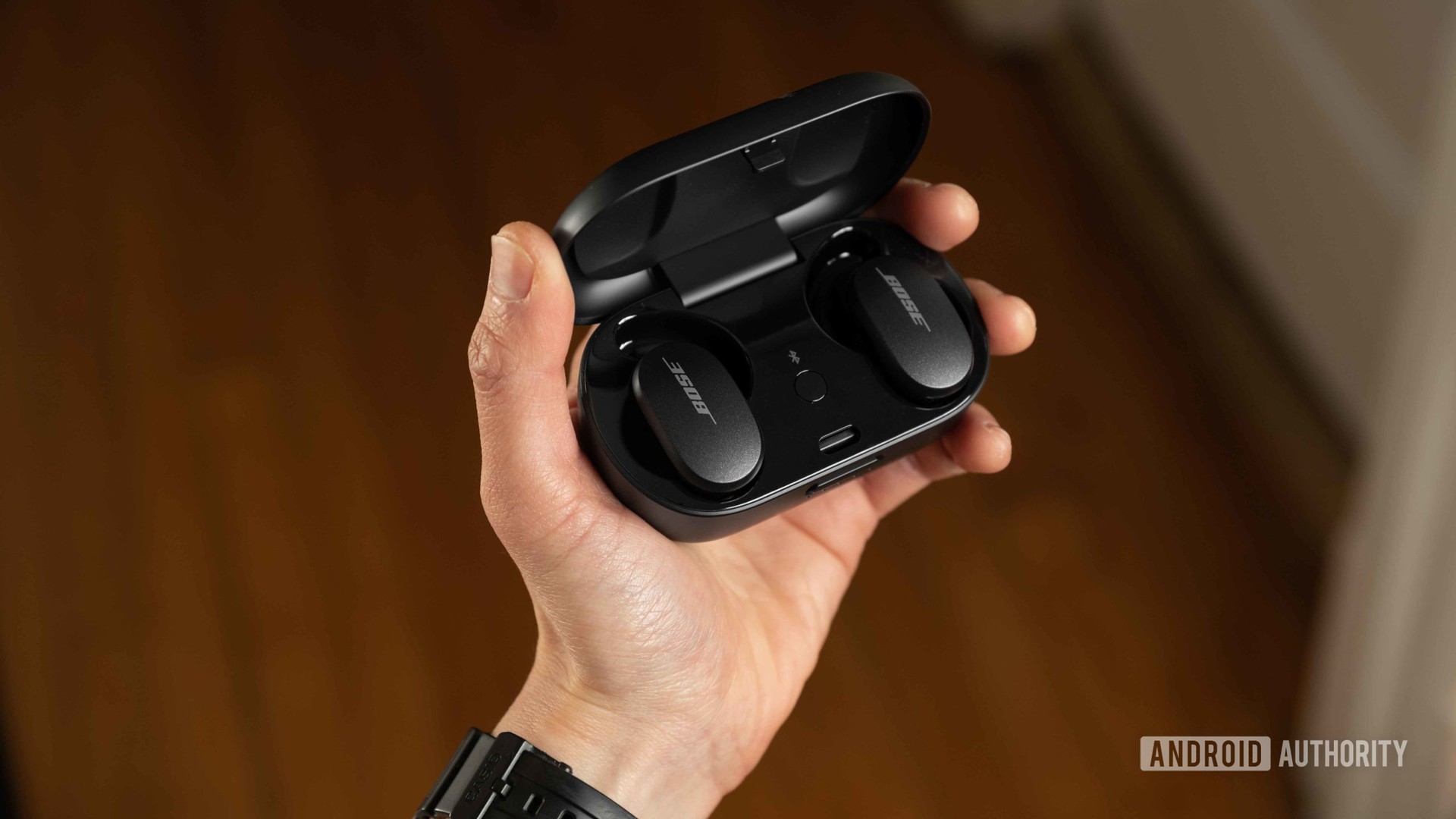 A hand holds the Bose QuietComfort Earbuds noise cancelling true wireless earbuds open charging case.