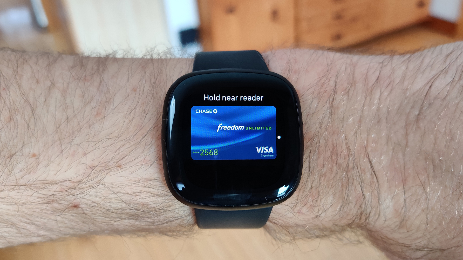 A Fitbit Versa 3 on a user's arm displays his Chase card on Fitbit Pay.