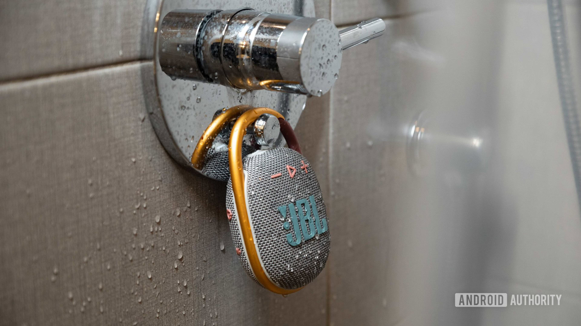 The JBL Clip 4 Bluetooth speaker hands from a shower as it's sprinkled by water.