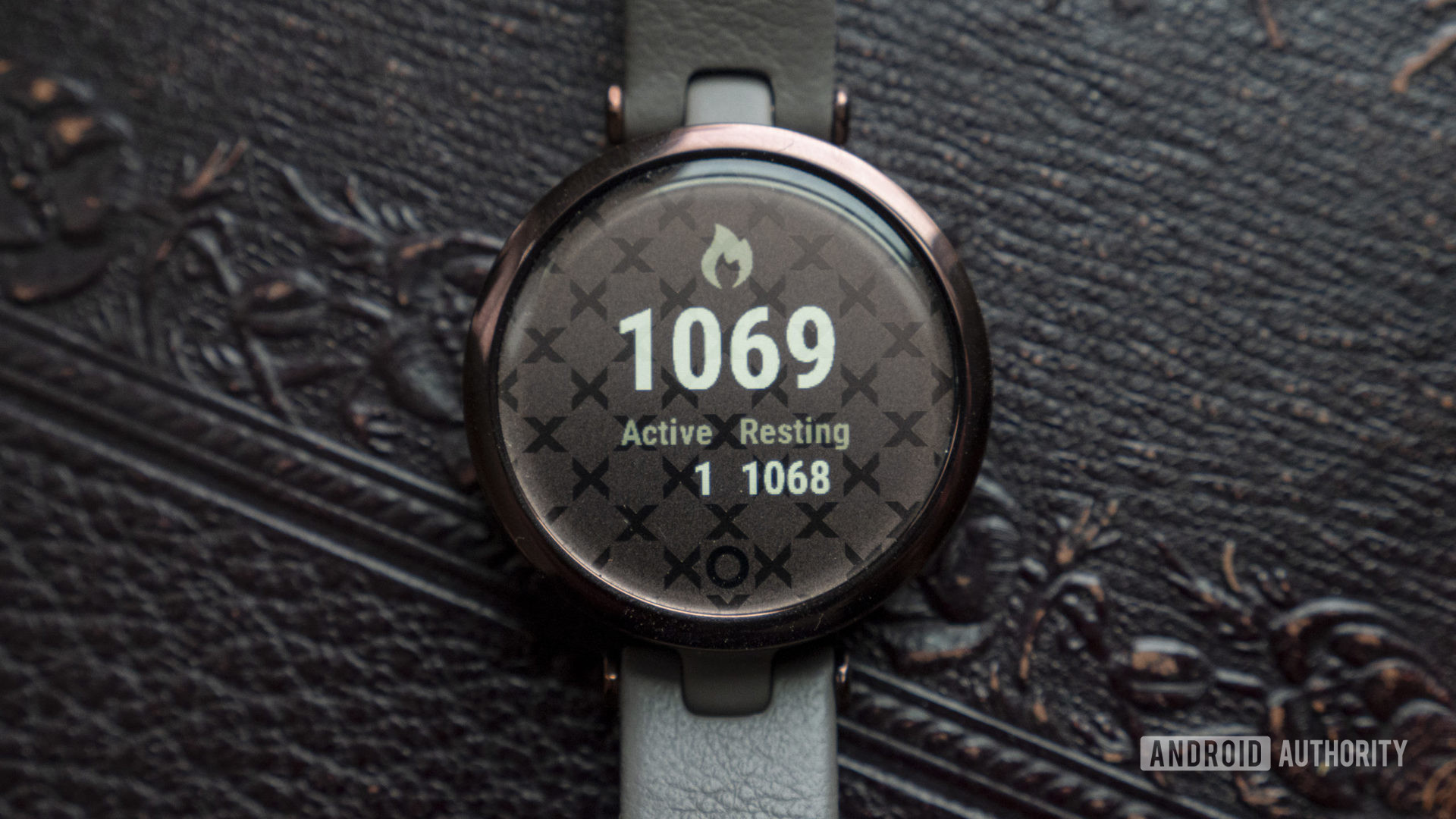 A Garmin Lily rests on a patterned leather serface, displaying a user's caloric burn.