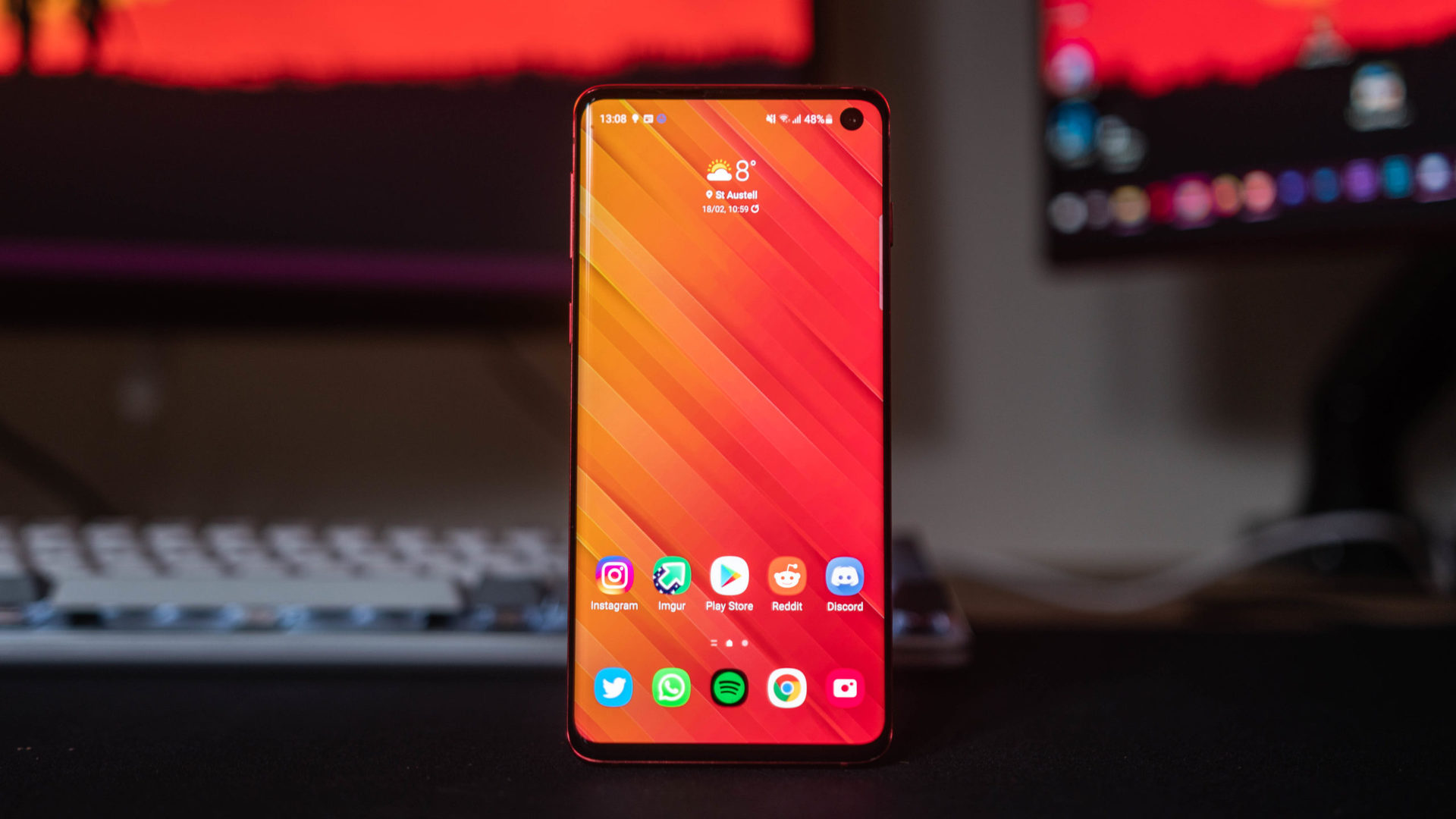 Samsung Galaxy S10 standing upright showing the home screen and app icons.