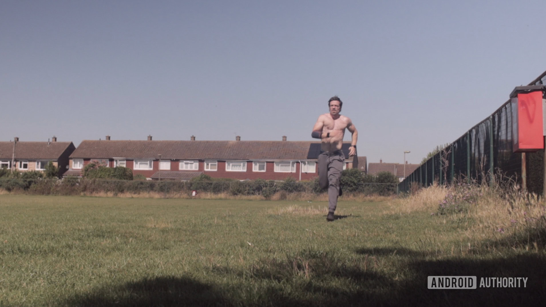A physically fit man runs shirtless along a fence line. 