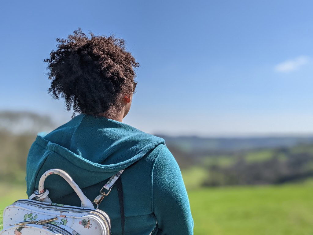 Google Pixel 5 camera bokeh 2 shot of the rear view of a woman with dark curly hair wearing a turquoise hoody with a backpack.