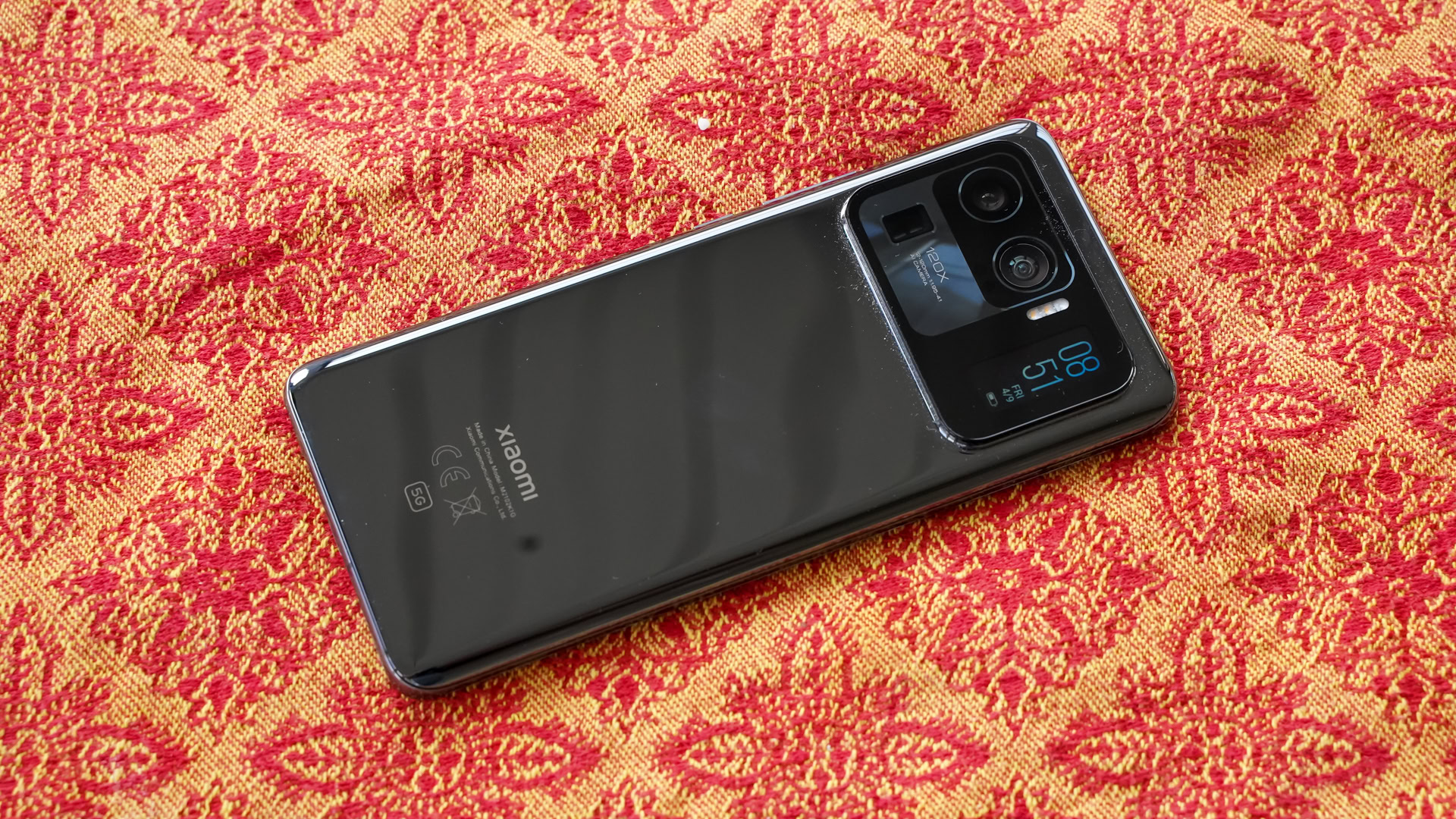 Xiaomi Mi 11 Ultra on a red and gold patterned background, showing the rear of the phone and camera module